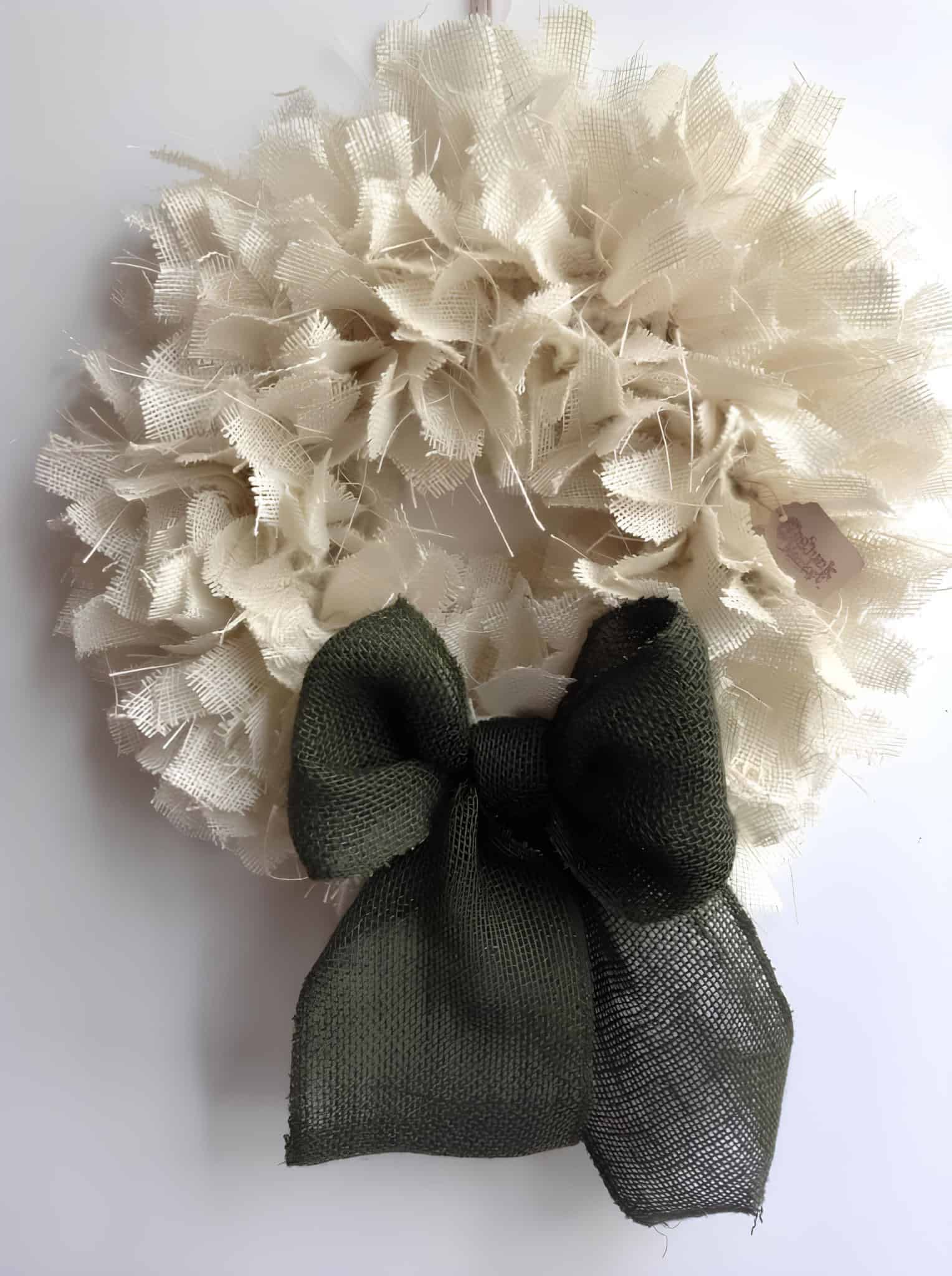 Neutral handmade Christmas wreath with frayed cream fabric and dark green bow