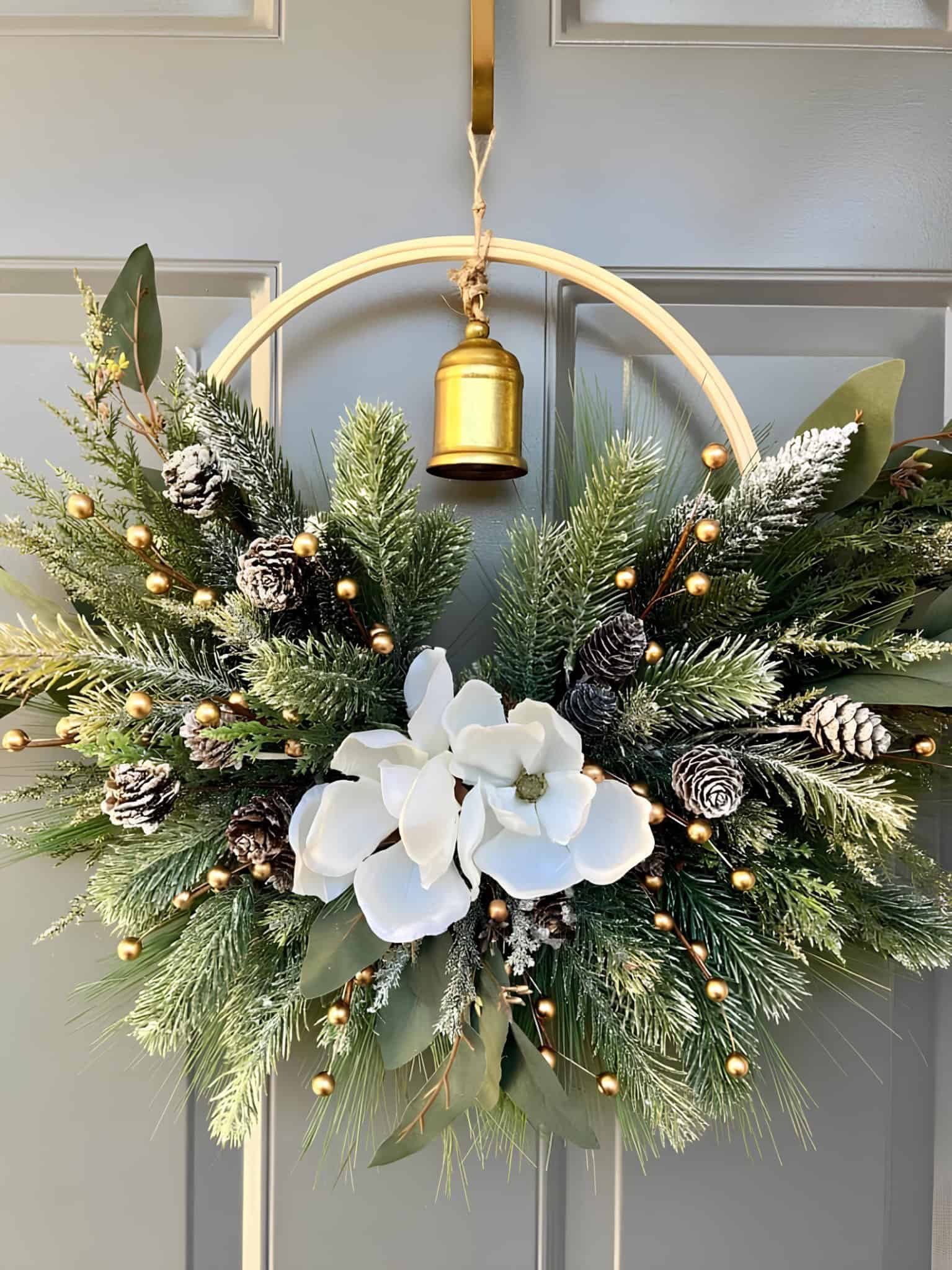 Elegant Christmas hoop wreath with magnolia blooms, frosted pine, and a gold bell