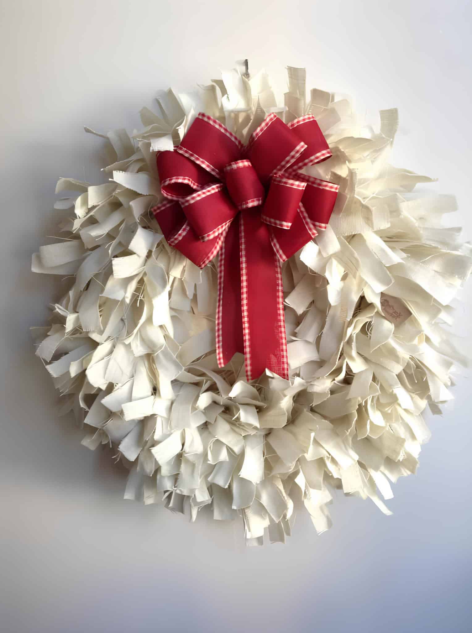 White rag wreath with a large red ribbon and gingham trim