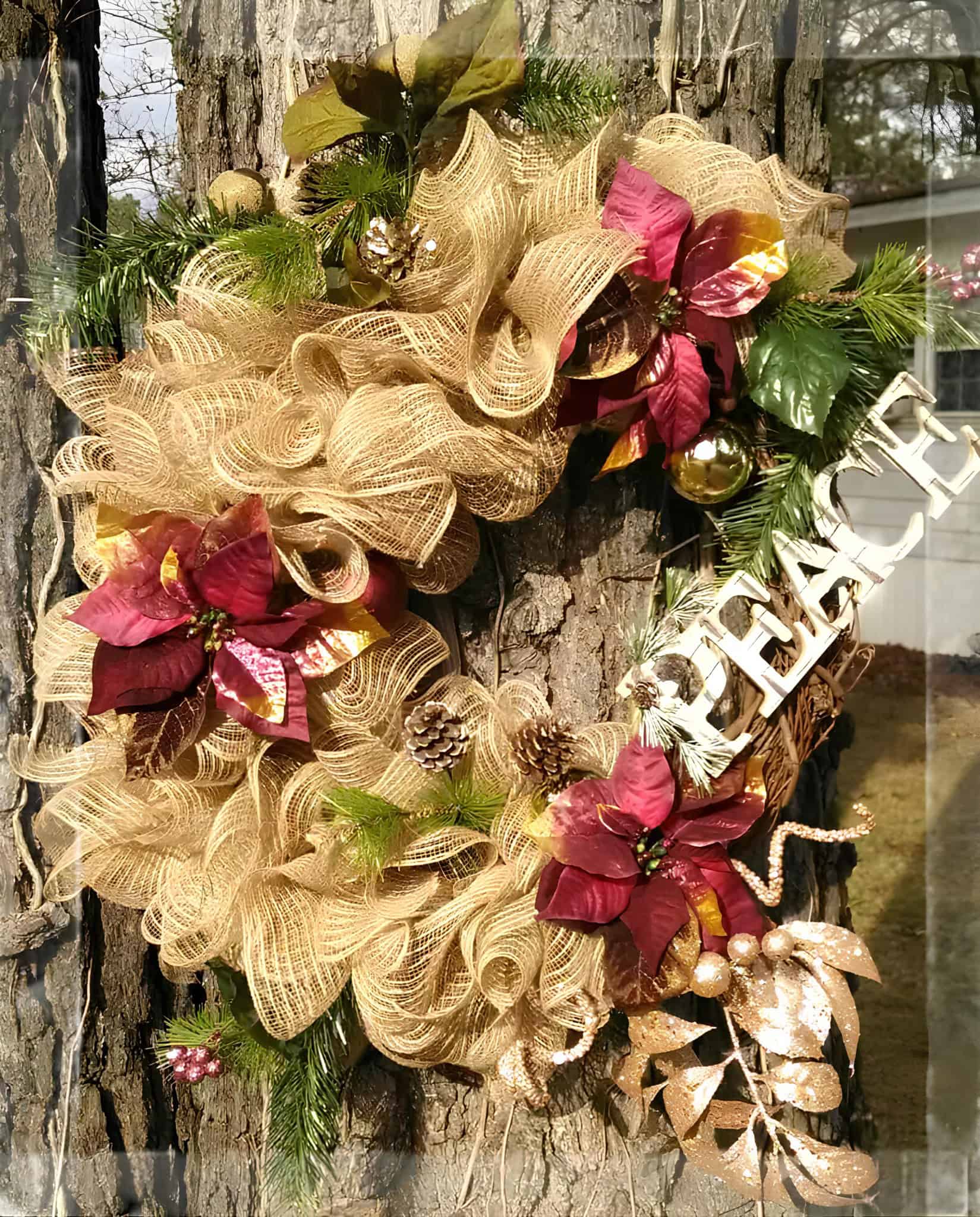 Gold ribbon wreath with red poinsettias and a peace sign accent
