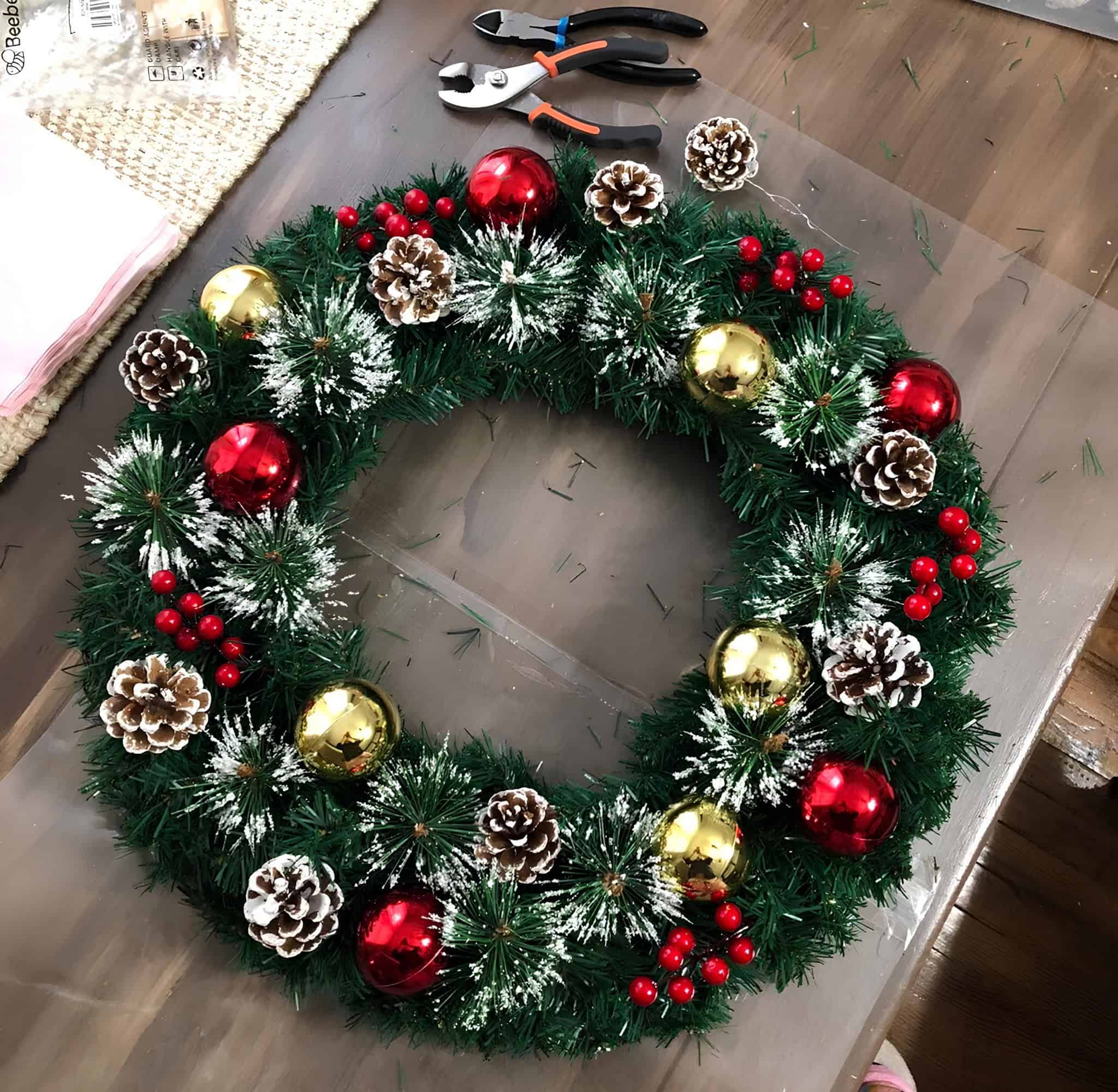 DIY Christmas wreath with gold and red ornaments, snow-frosted pinecones, and red berries