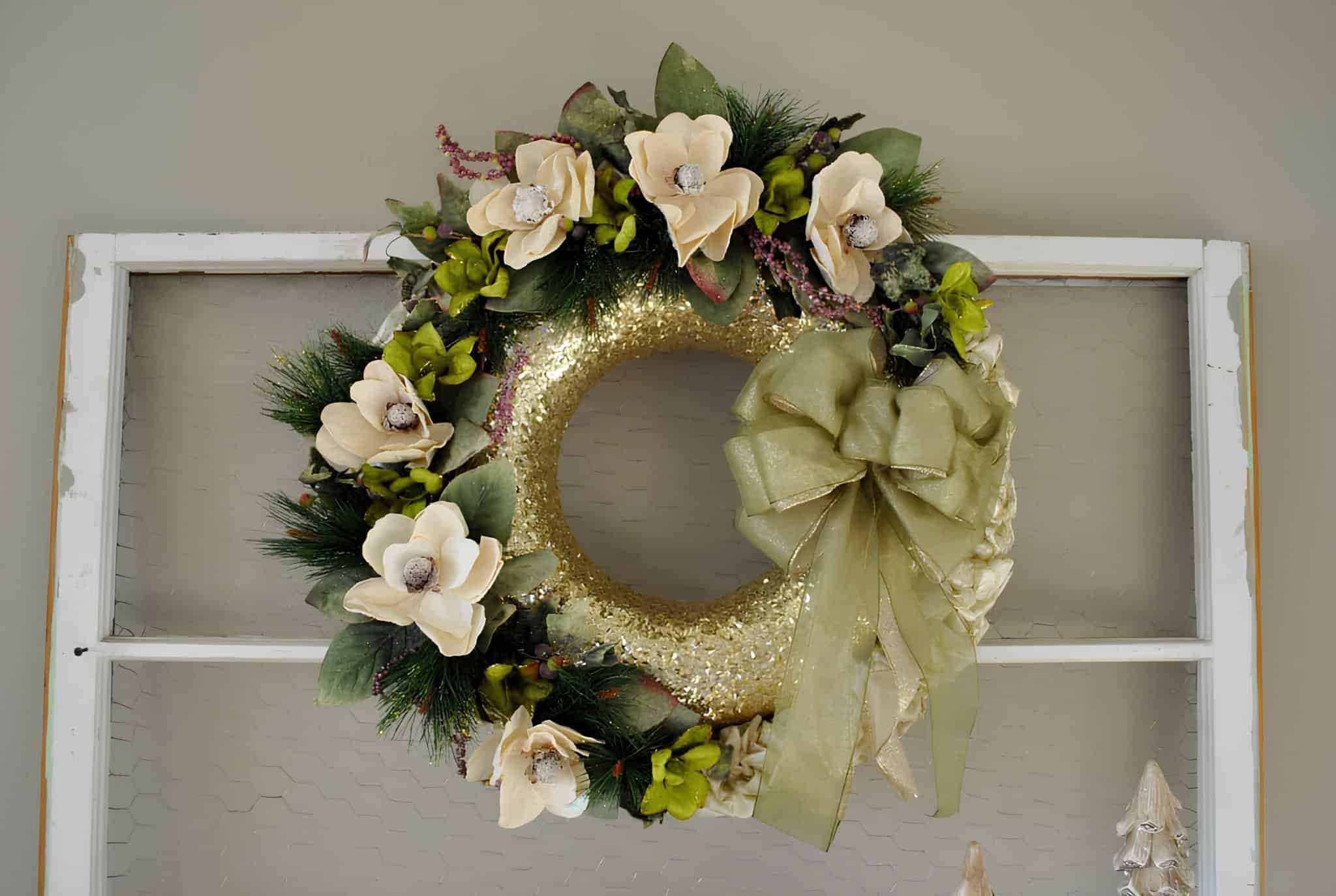 Gold glittered Christmas wreath decorated with cream flowers and green bow