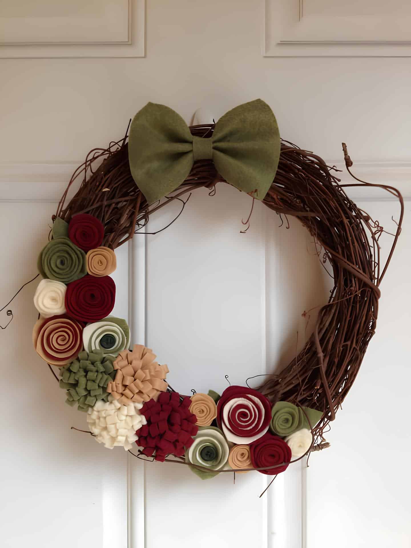 Grapevine wreath decorated with felt flowers and a large green bow