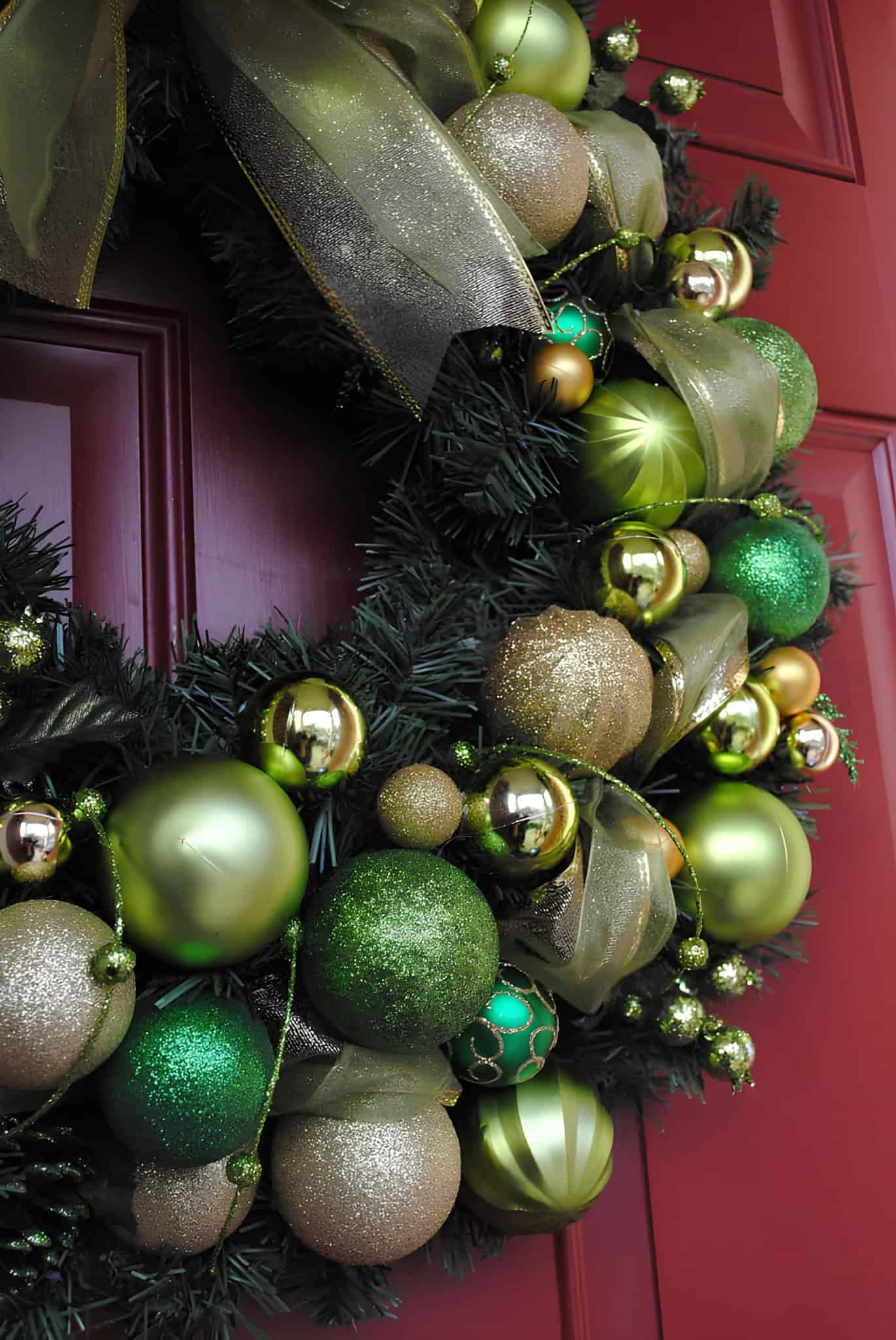 Green and gold ornament Christmas wreath with sheer ribbon on a red door