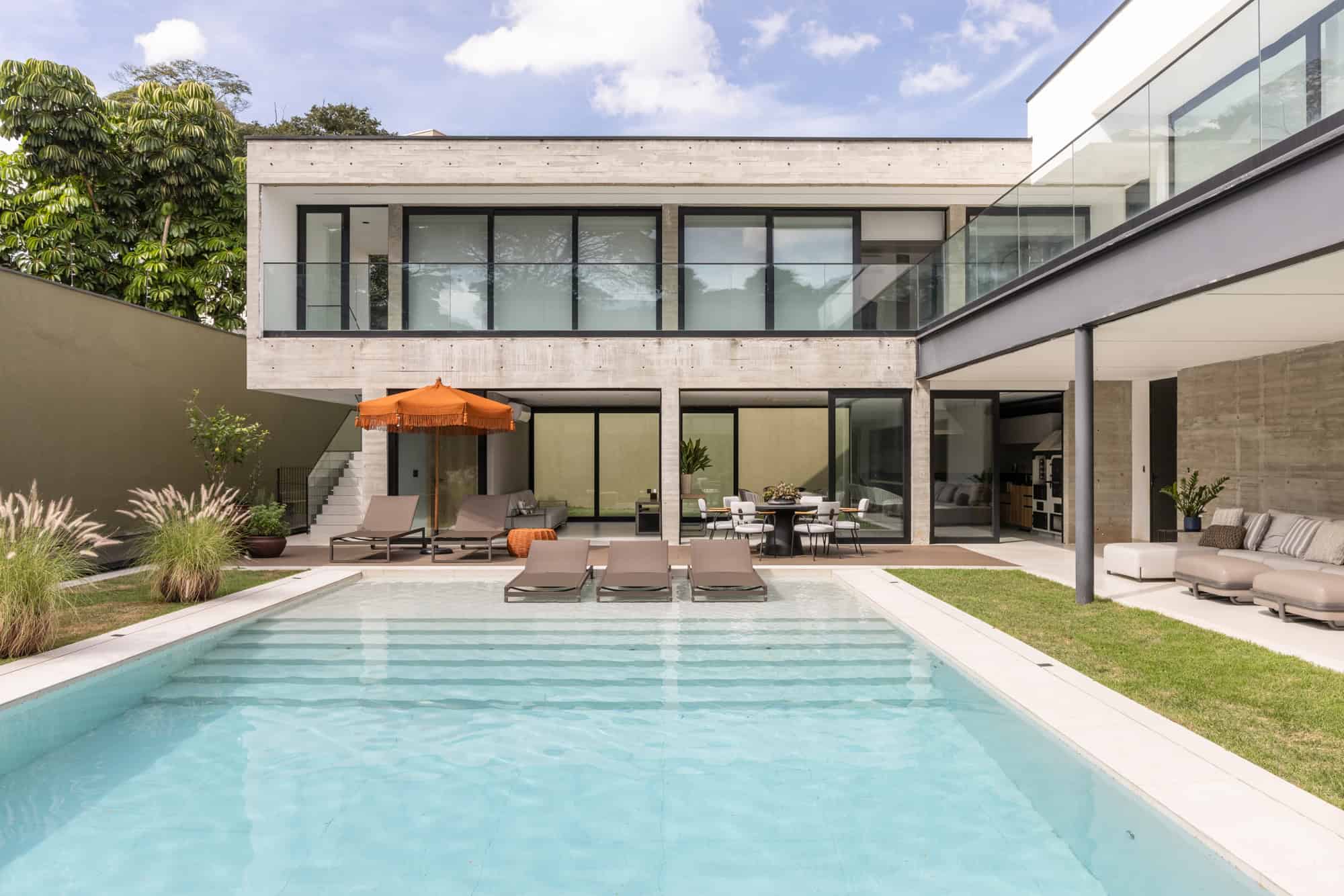 Modern luxury house with minimalist concrete architecture and large glass windows, outdoor pool, and stylish patio furniture, perfect for contemporary home design and outdoor living.