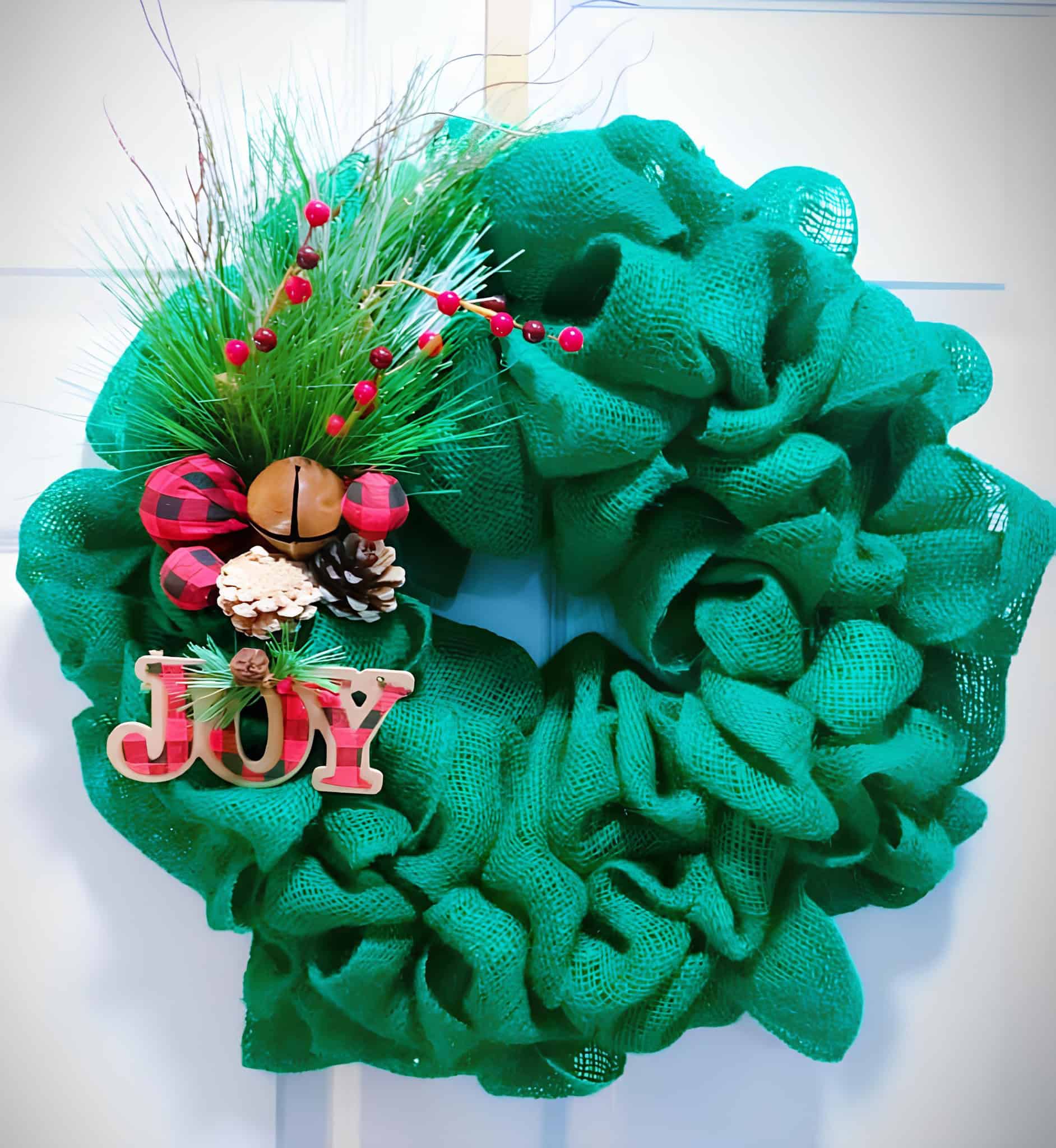 Green burlap Christmas wreath with JOY sign, buffalo plaid accents, pine and jingle bell