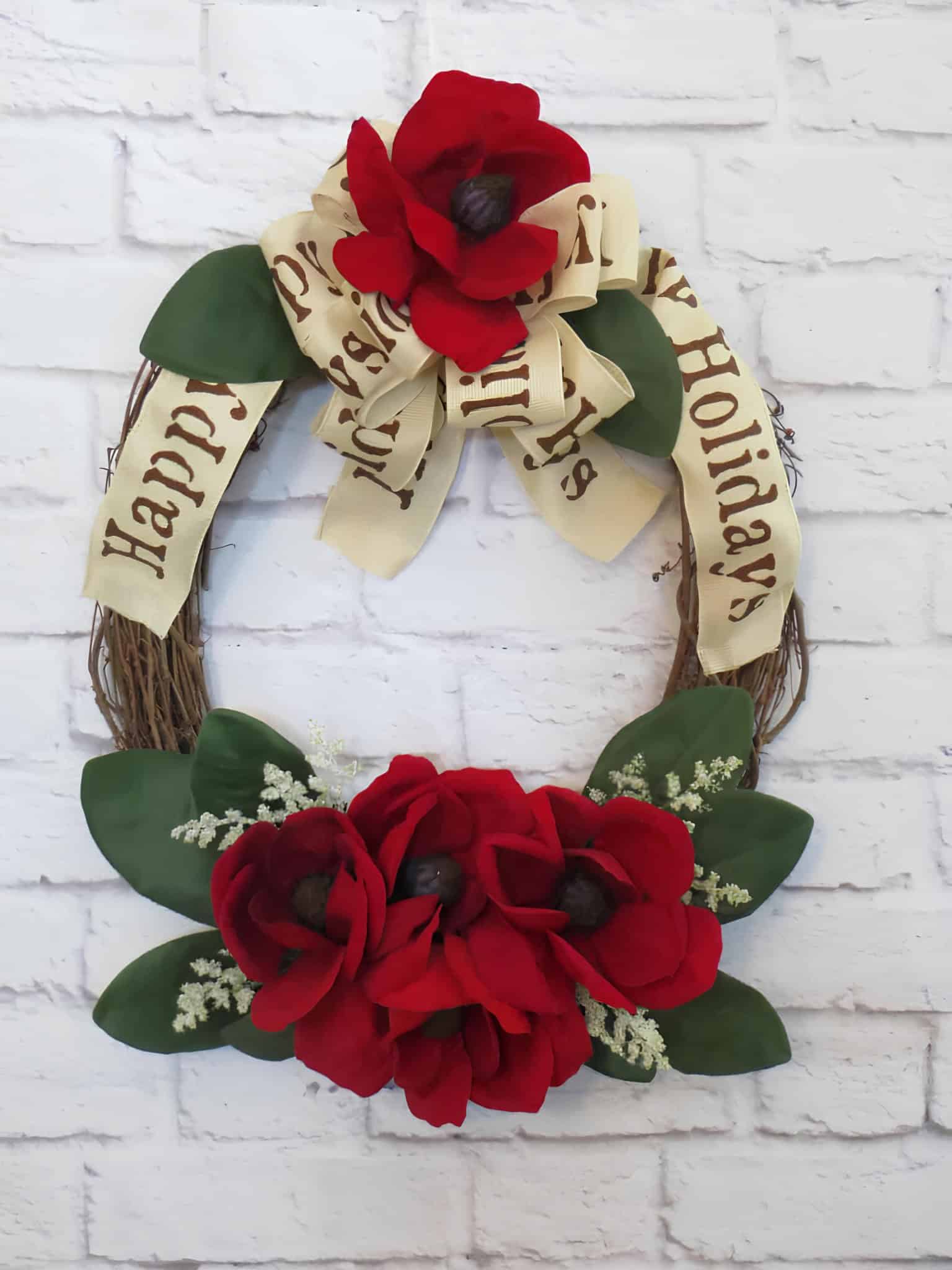 Magnolia flower Christmas wreath with holiday ribbon and red floral accents