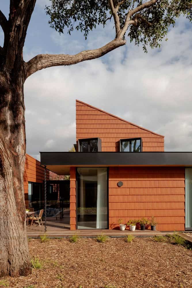 Mahogany House Facade Gable by R ARCHITECTURE Modern contemporary house with angular roof design, featuring natural brick exterior, large glass doors, and lush outdoor landscaping, exemplifying innovative architecture and unique design trends.