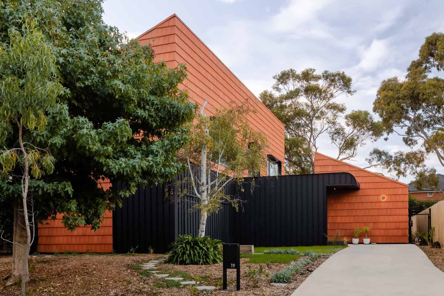 Contemporary modern house with striking red brick exterior, black metal gate, lush greenery, and minimalist landscaping, showcasing innovative architectural design and stylish outdoor aesthetic.