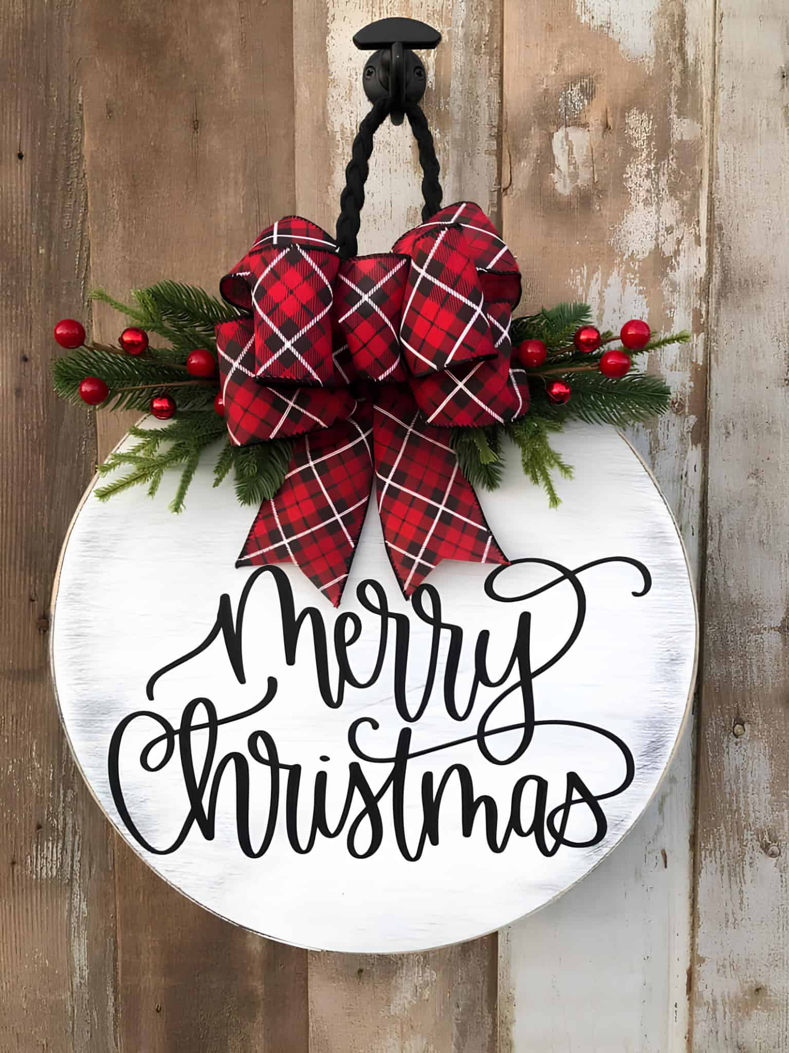 White round Merry Christmas wood sign with red plaid bow and evergreens