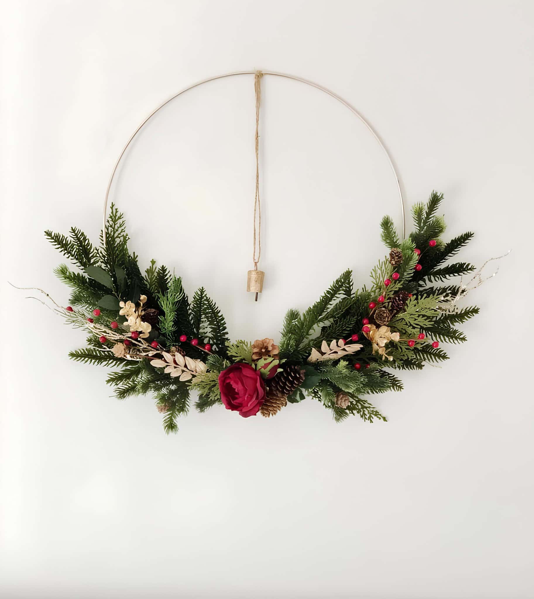 Minimal metal hoop wreath with winter greenery, pinecones and a single red rose
