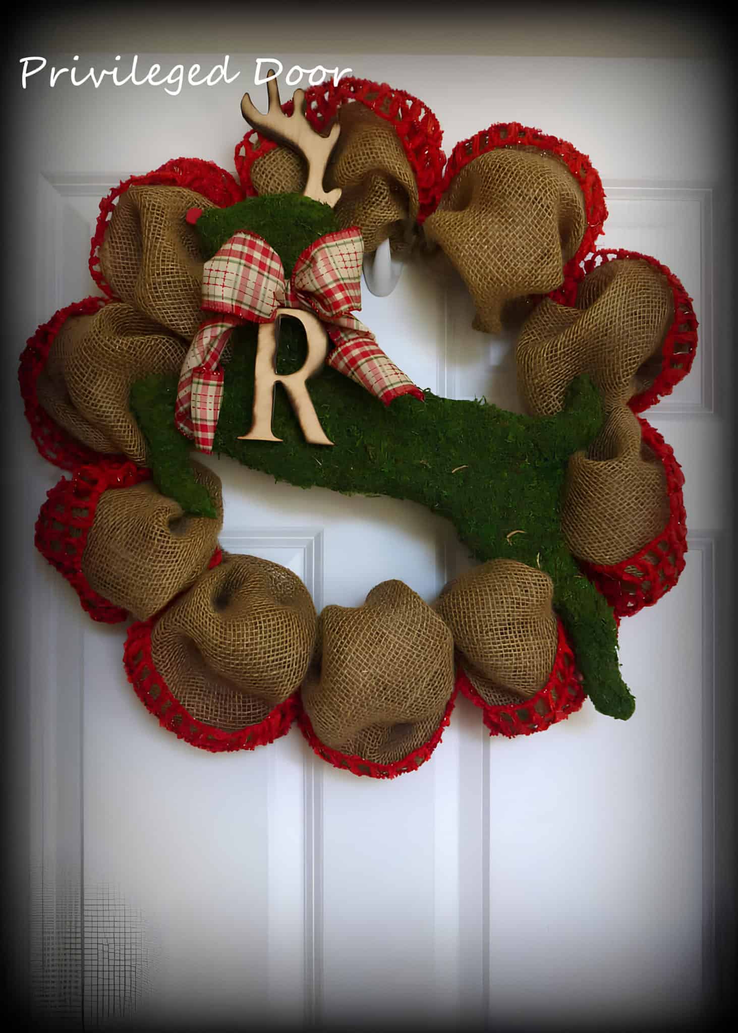 Burlap wreath with red-trimmed edges and a moss reindeer silhouette with plaid bow and monogram