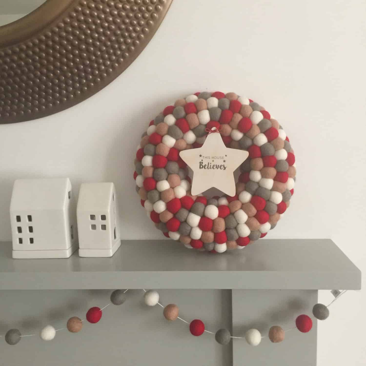 Neutral red, gray and ivory pom pom Christmas wreath with a wooden star tag on a mantle