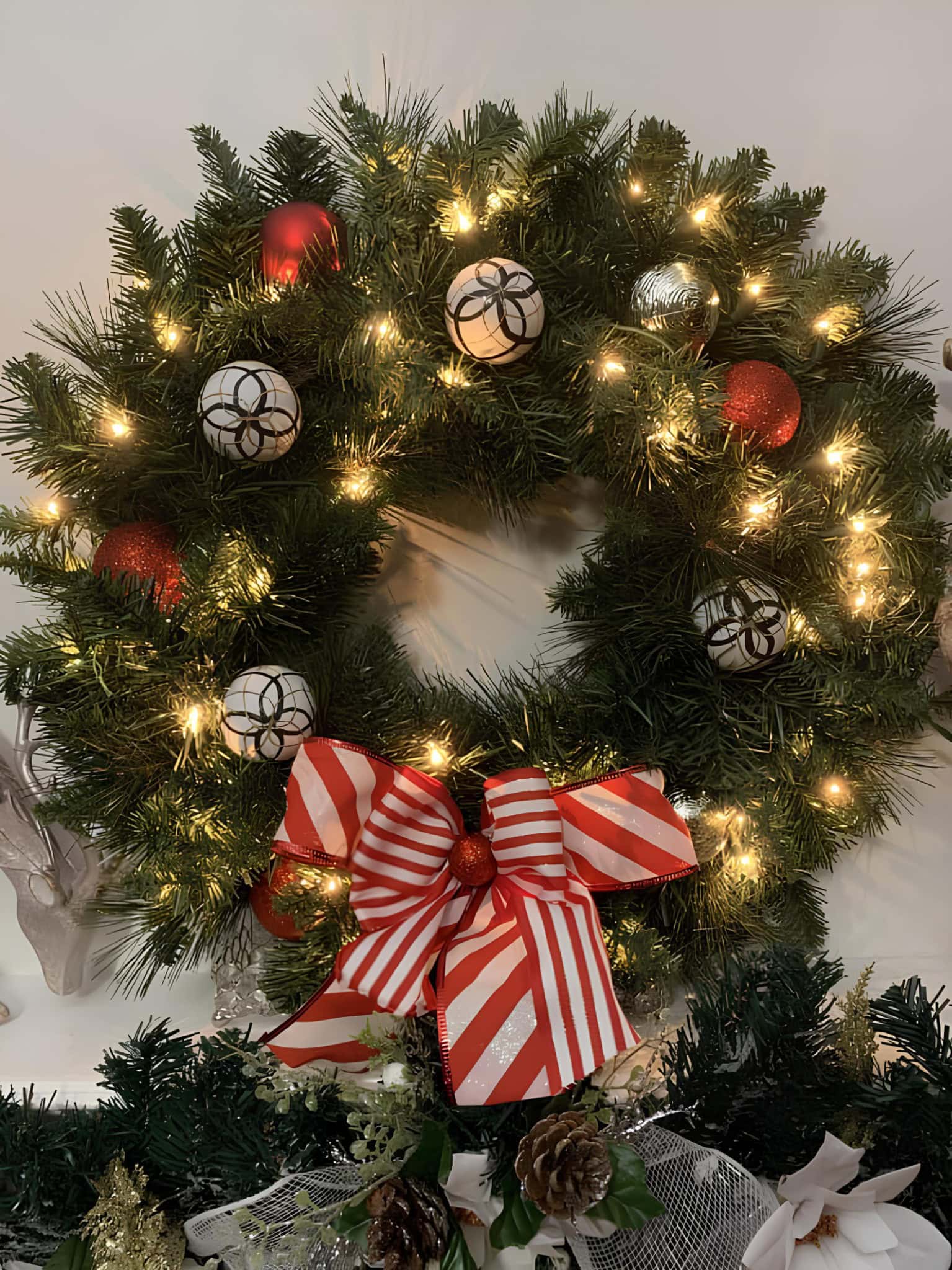 Lighted pine wreath with ornaments and a peppermint candy–stripe bow