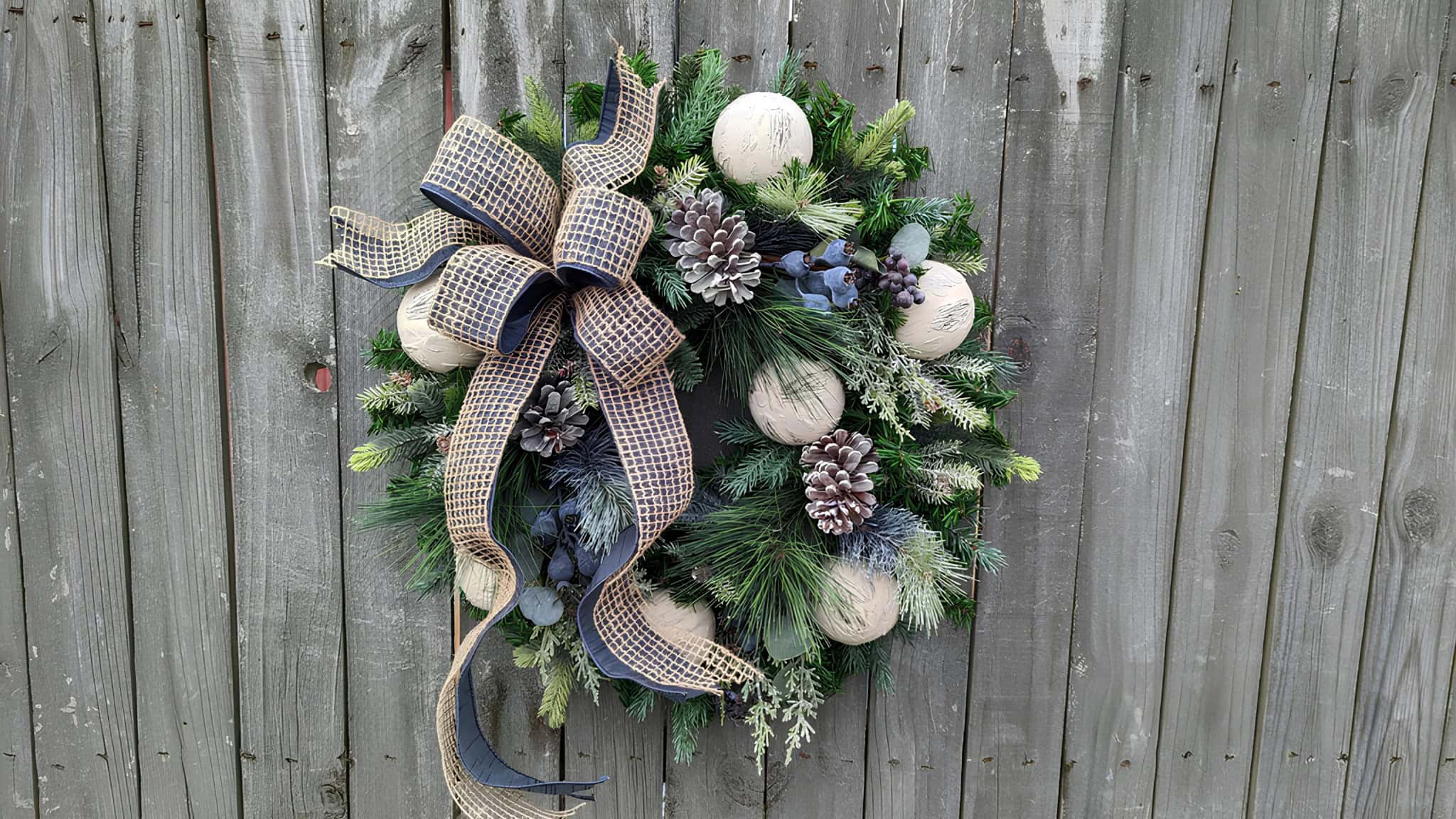 Rustic pine wreath with neutral ornaments, frosted cones and navy ribbon