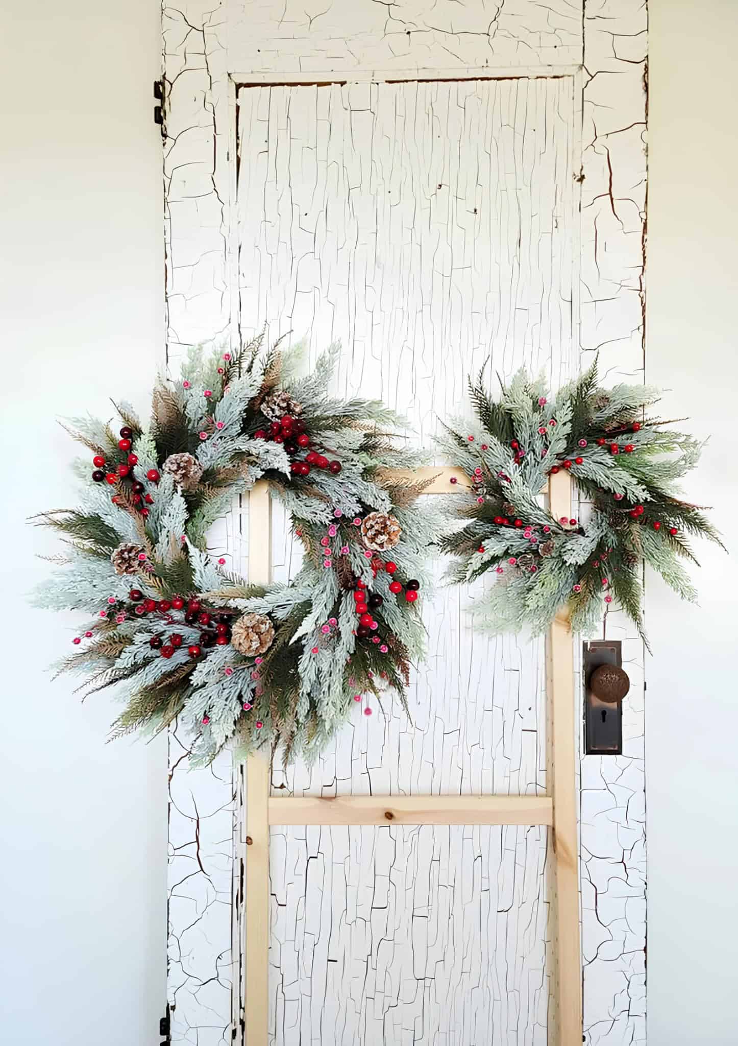 Pair of frosted cedar wreaths with red berries and pinecones
