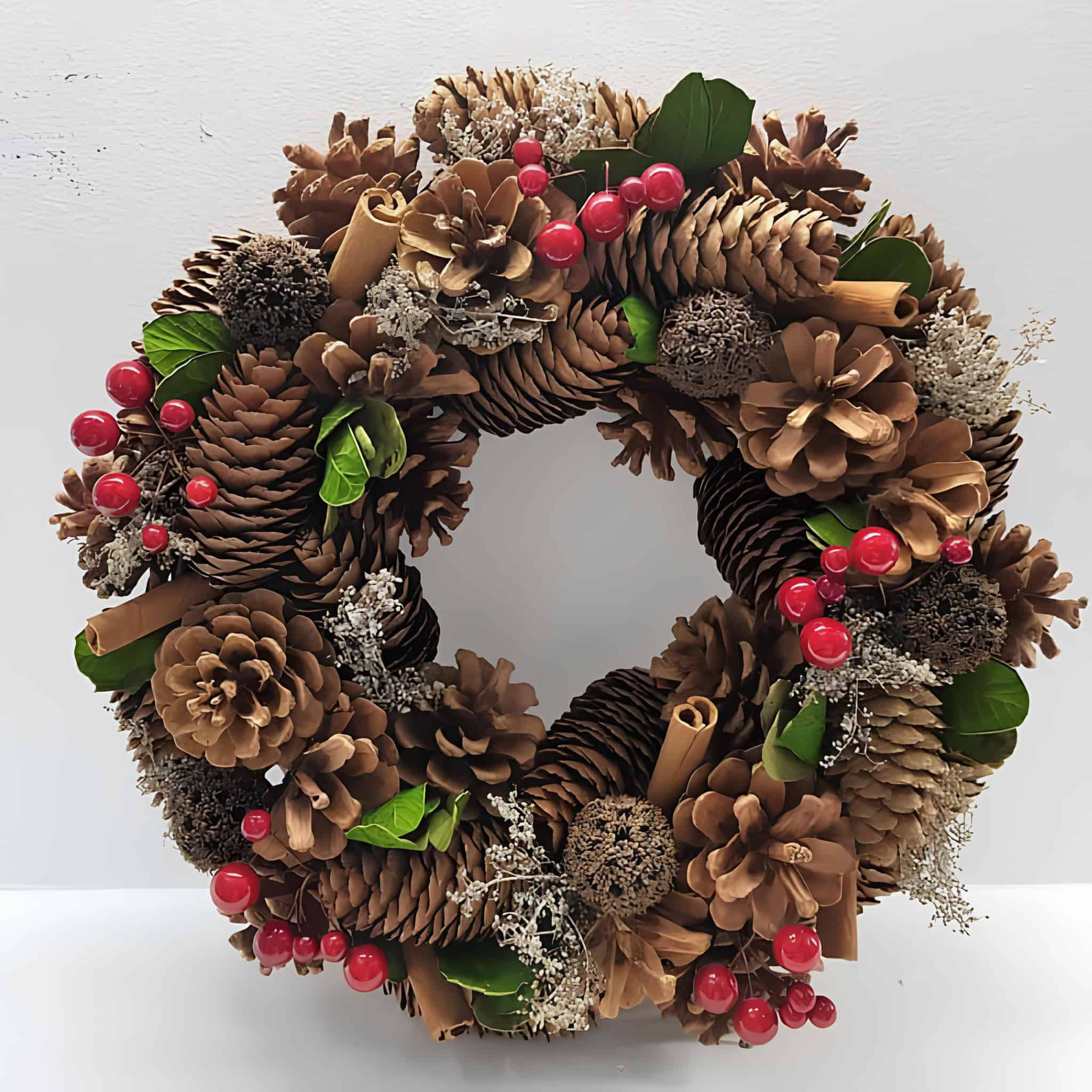Pinecone Christmas wreath decorated with cinnamon sticks, red berries, and greenery