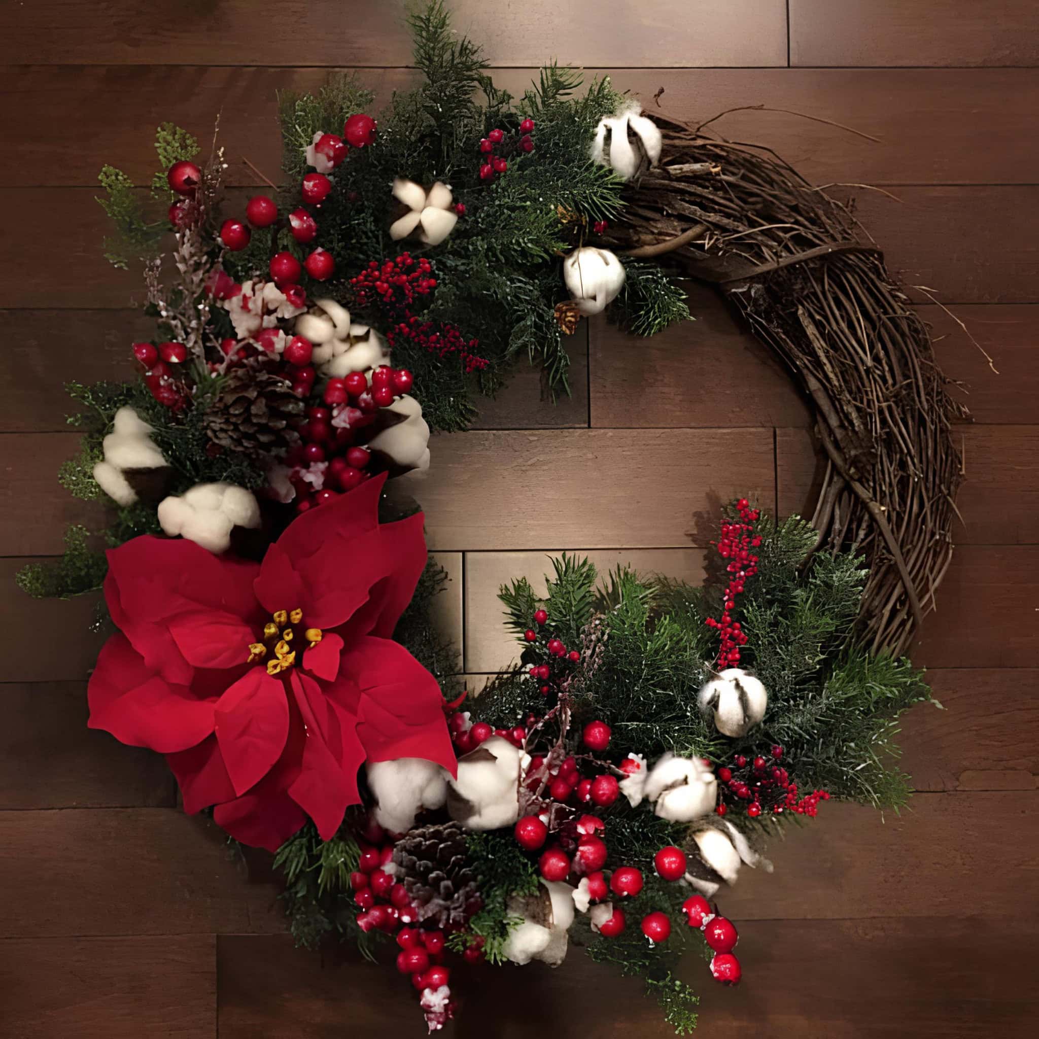 Grapevine wreath with a red poinsettia, cotton bolls, berries, pinecones and greenery tied with a bow
