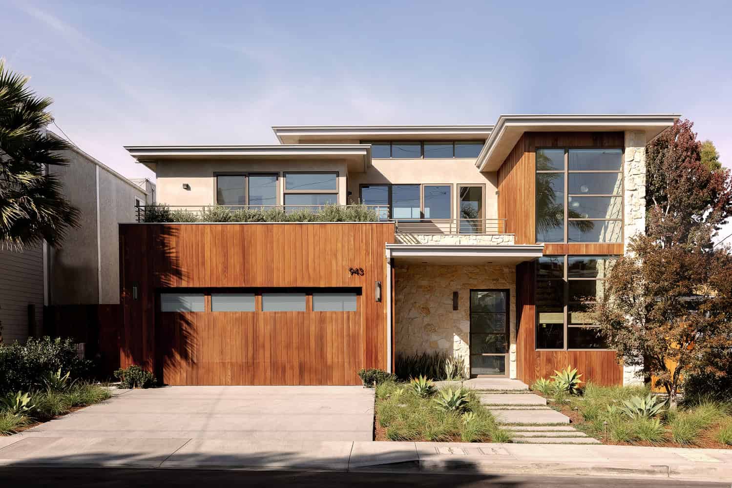 Contemporary modern house with sleek architectural design, featuring wood paneling, large glass windows, and lush landscaping, showcasing innovative architecture and home design.
