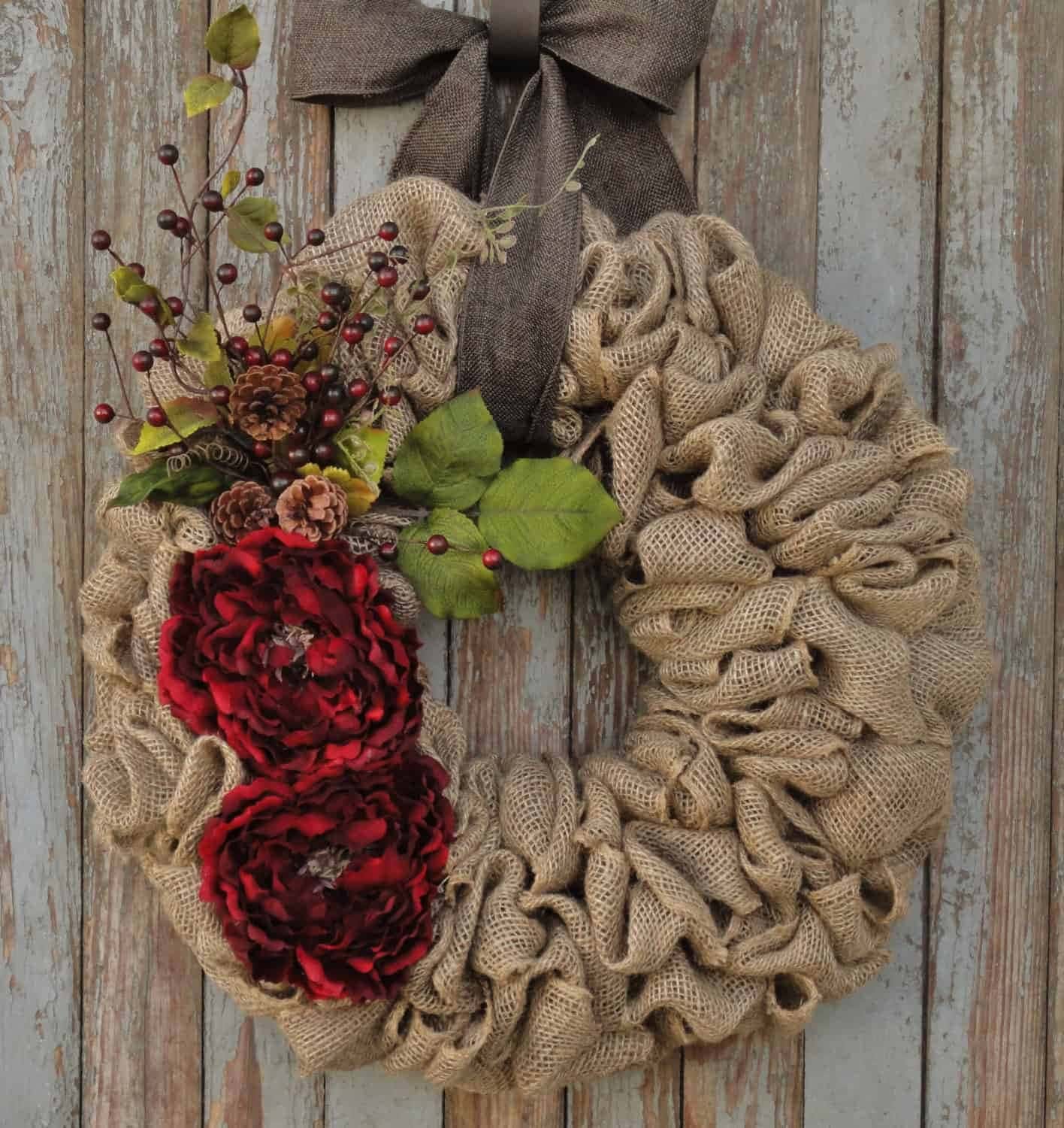 Burlap wreath with red flowers, pinecones, greenery, and brown bow