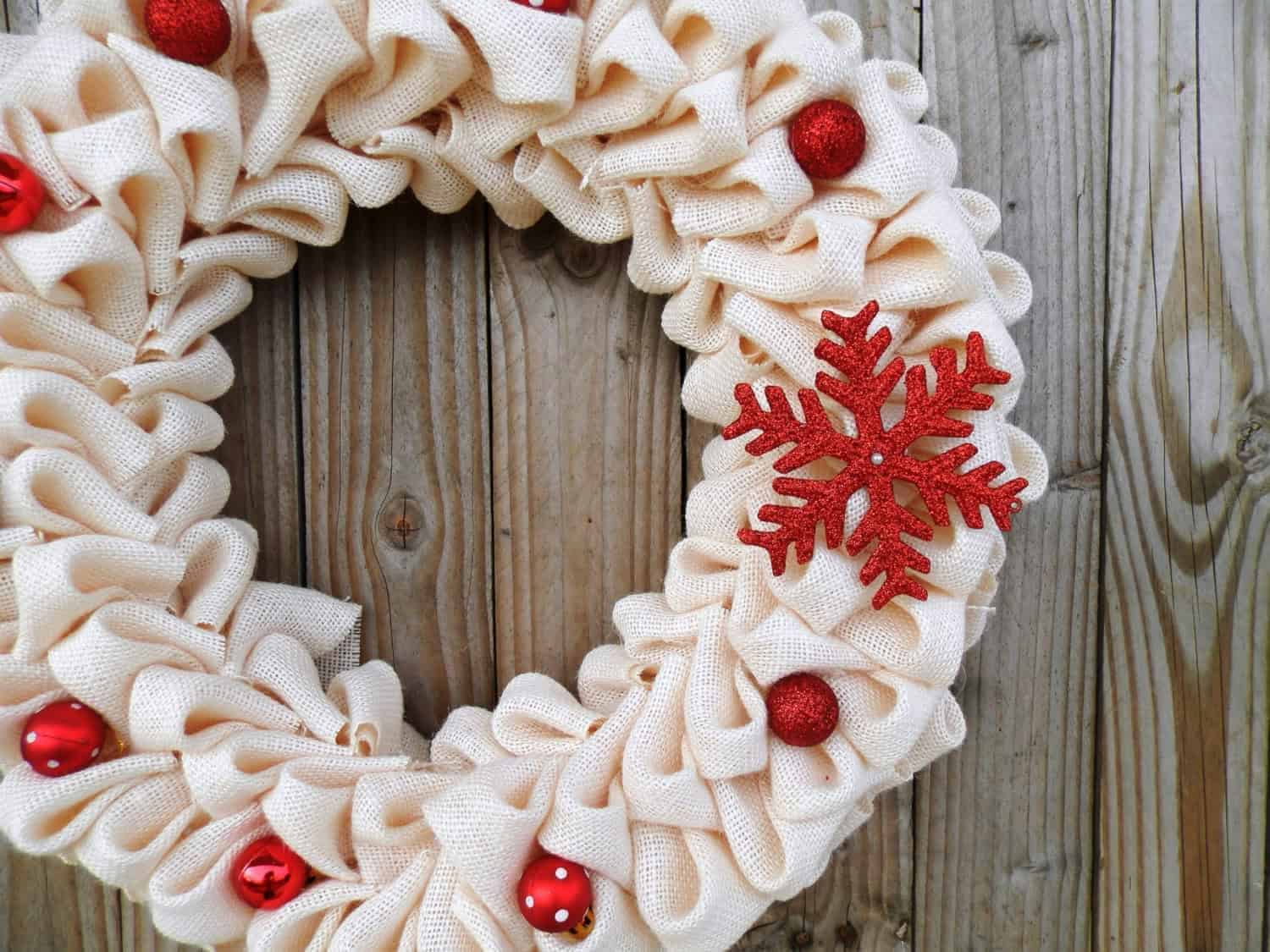 Festive fabric Christmas wreath with red ornaments and a red snowflake decoration on a rustic wooden background.