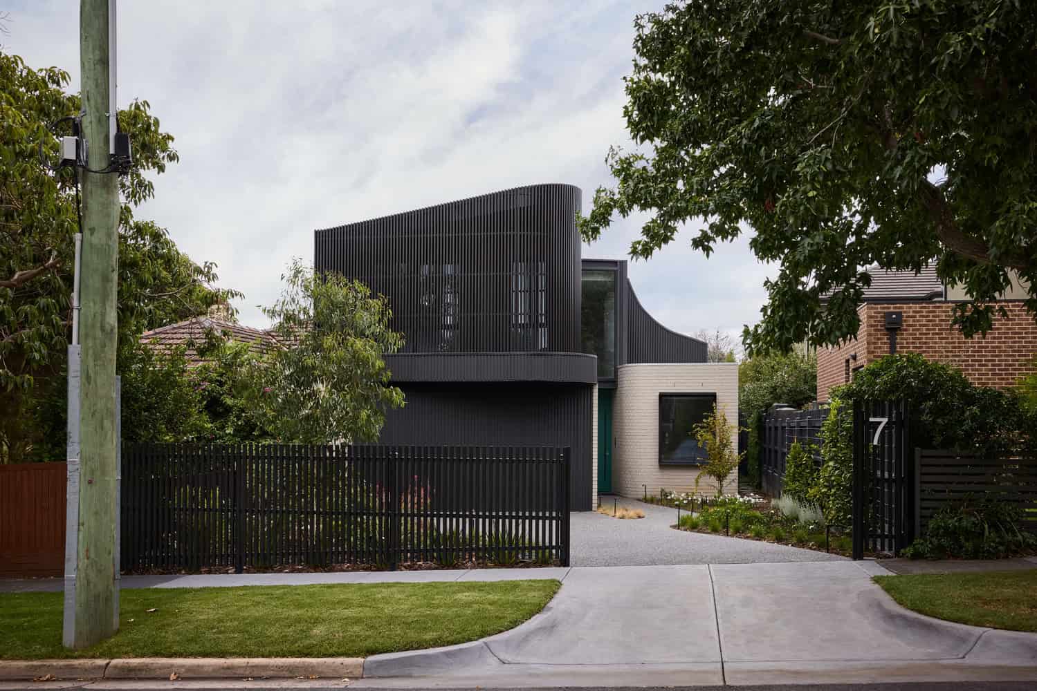 Contemporary black and white modern house with sleek architectural design, featuring curved black slatted facade and minimalist landscaping.