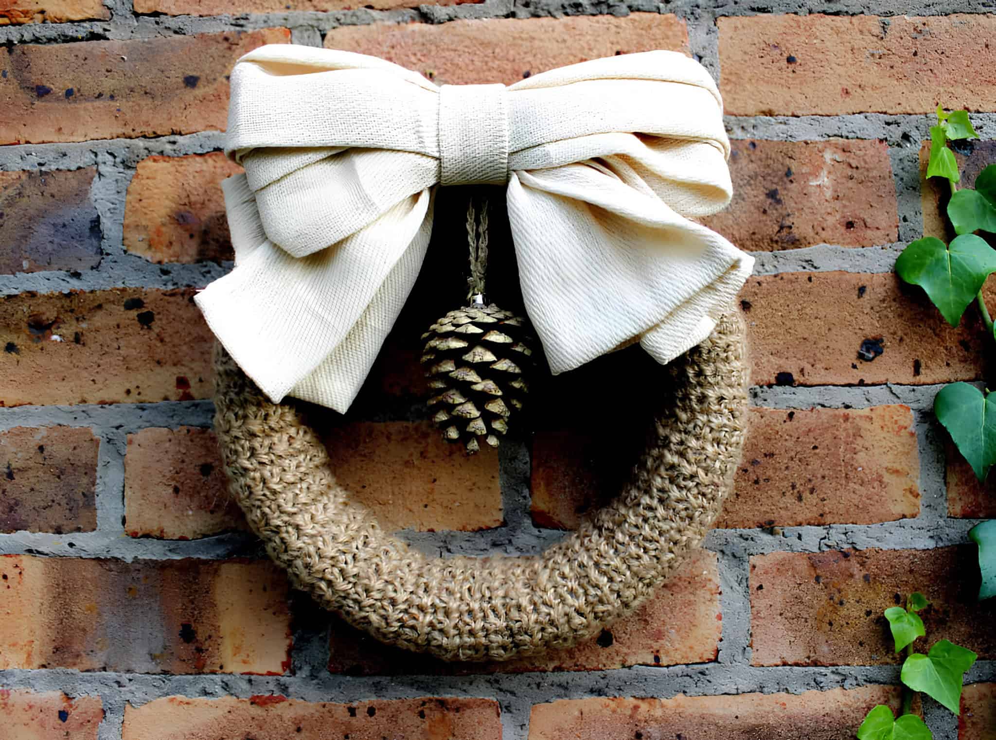 Handmade burlap wreath with an oversized cream bow and hanging pinecone