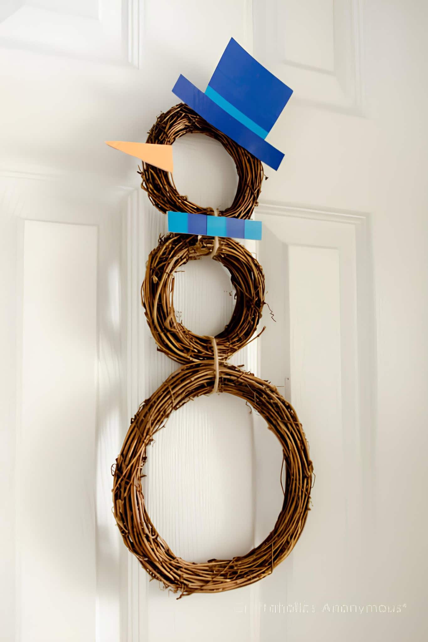 Three-ring grapevine snowman wreath with blue top hat, carrot nose, and blue scarf accent