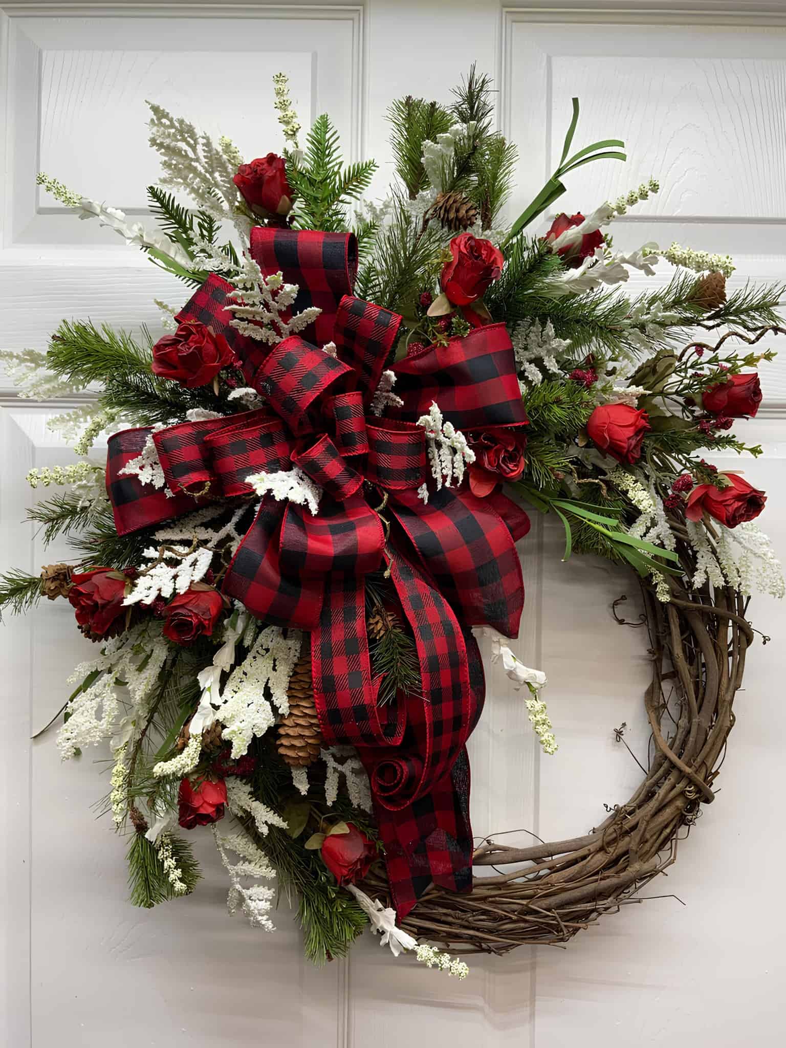 Rustic wooden Christmas wreath with red roses, buffalo plaid bow, pinecones and winter greens