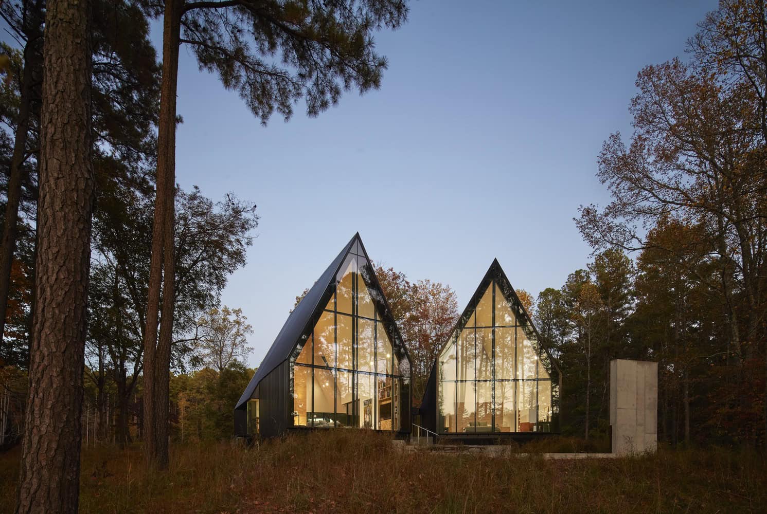 Modern glass A-frame cabin nestled in a forest with tall trees, showcasing contemporary architecture, sleek design, and seamless integration with natural surroundings, perfect for nature lovers.