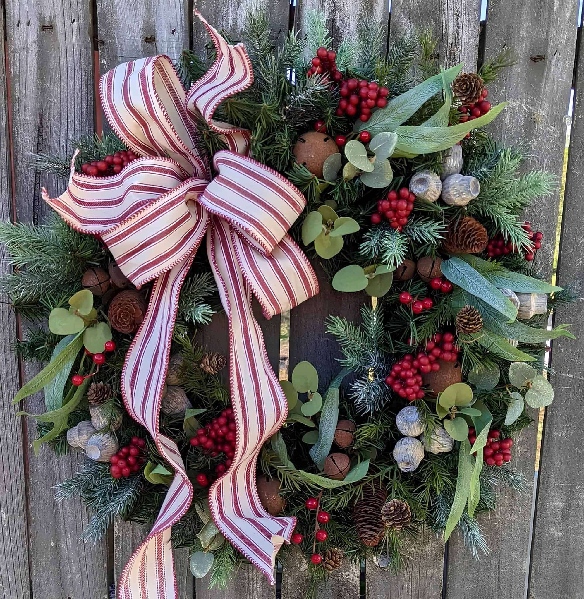 Christmas wreath with striped bow, red berries, pinecones, and frosted greenery