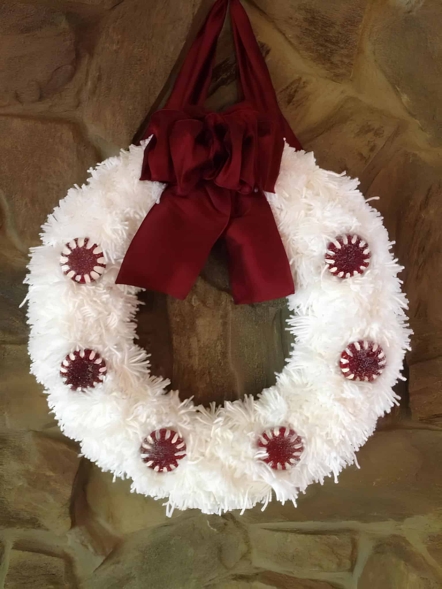 Festive white Christmas wreath with burgundy ribbon and peppermint candy details