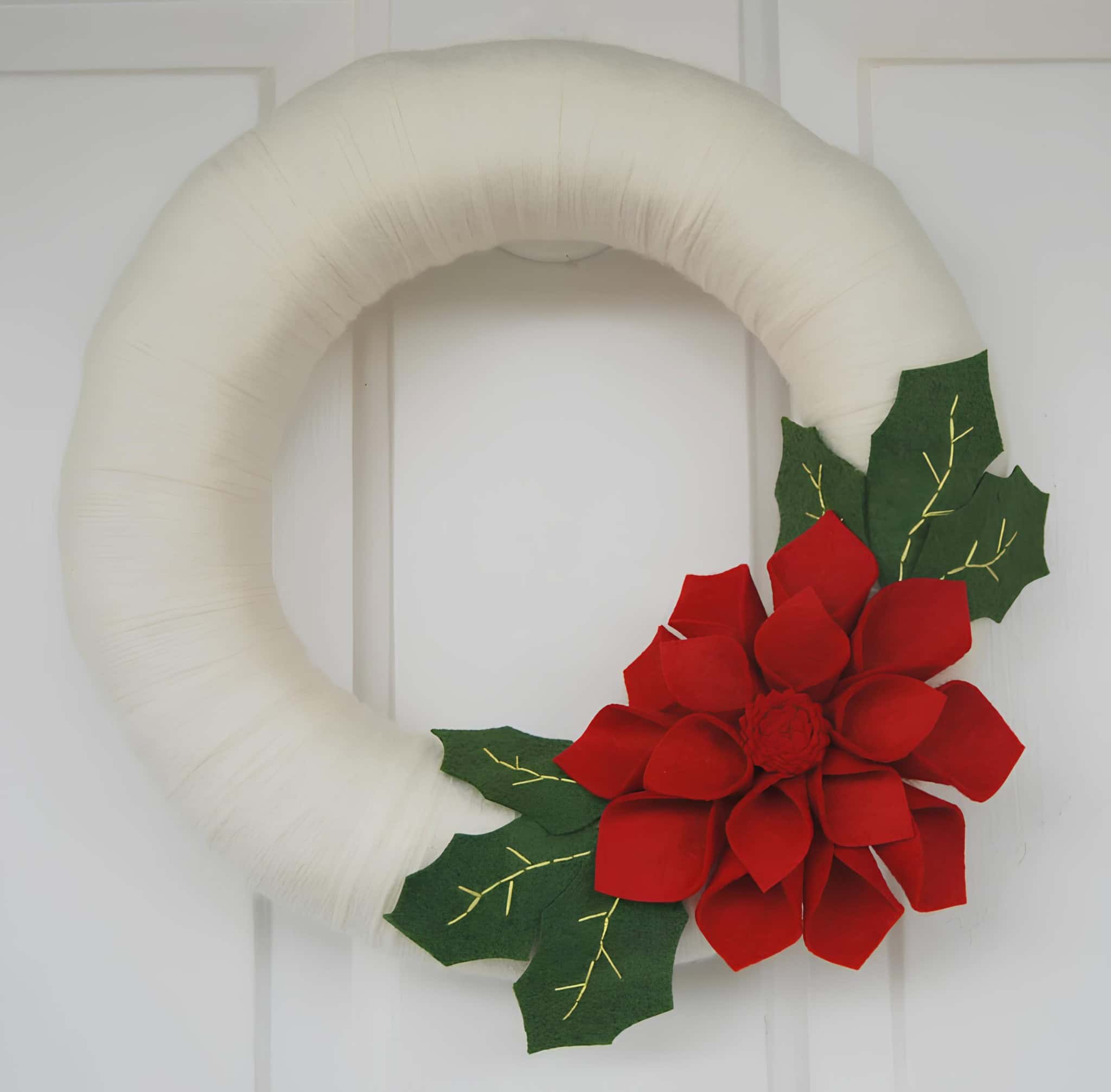 Minimalist white felt Christmas wreath with red poinsettia flower and green leaves
