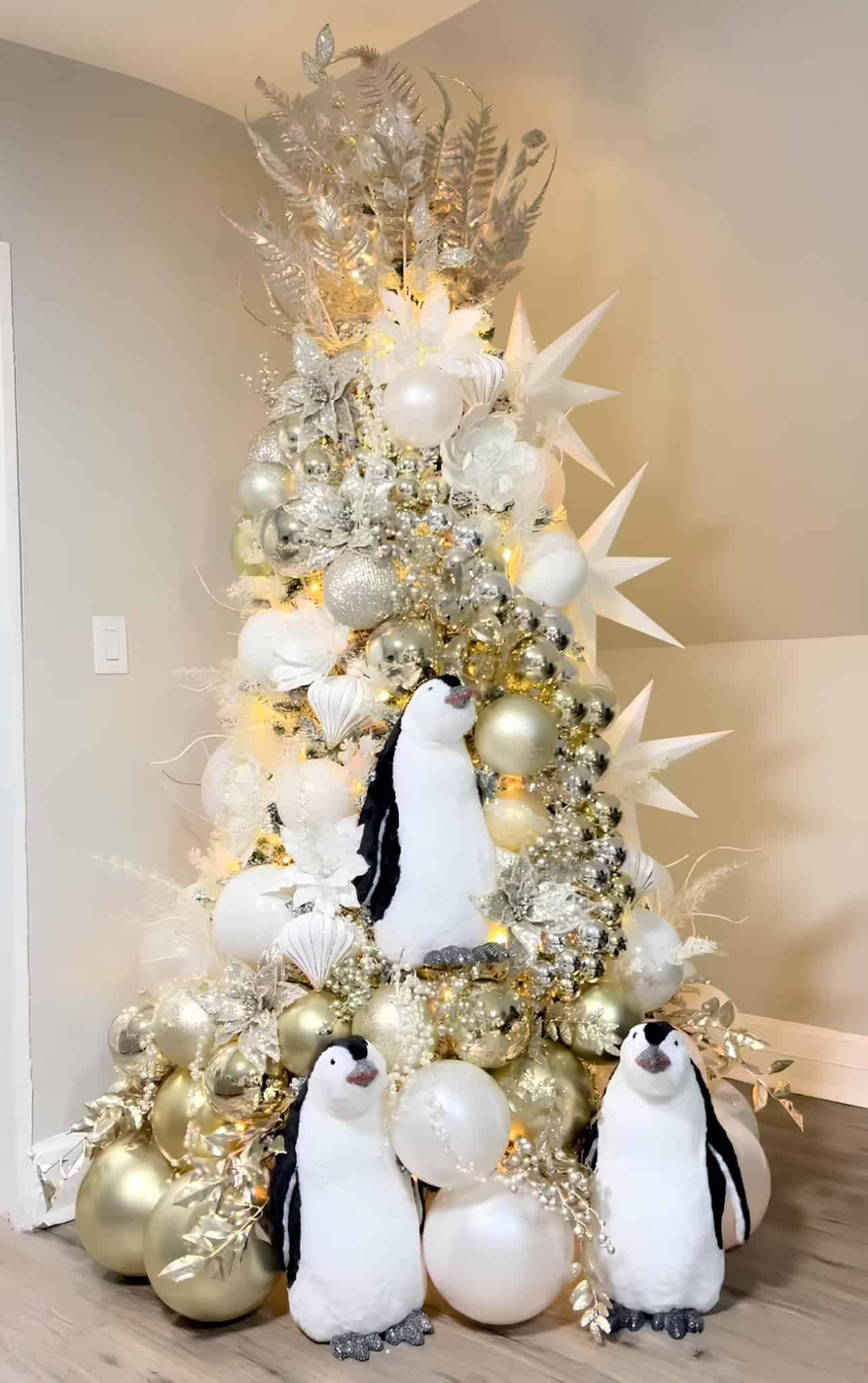 White and gold Christmas tree with penguin decorations and glittering metallic ornaments