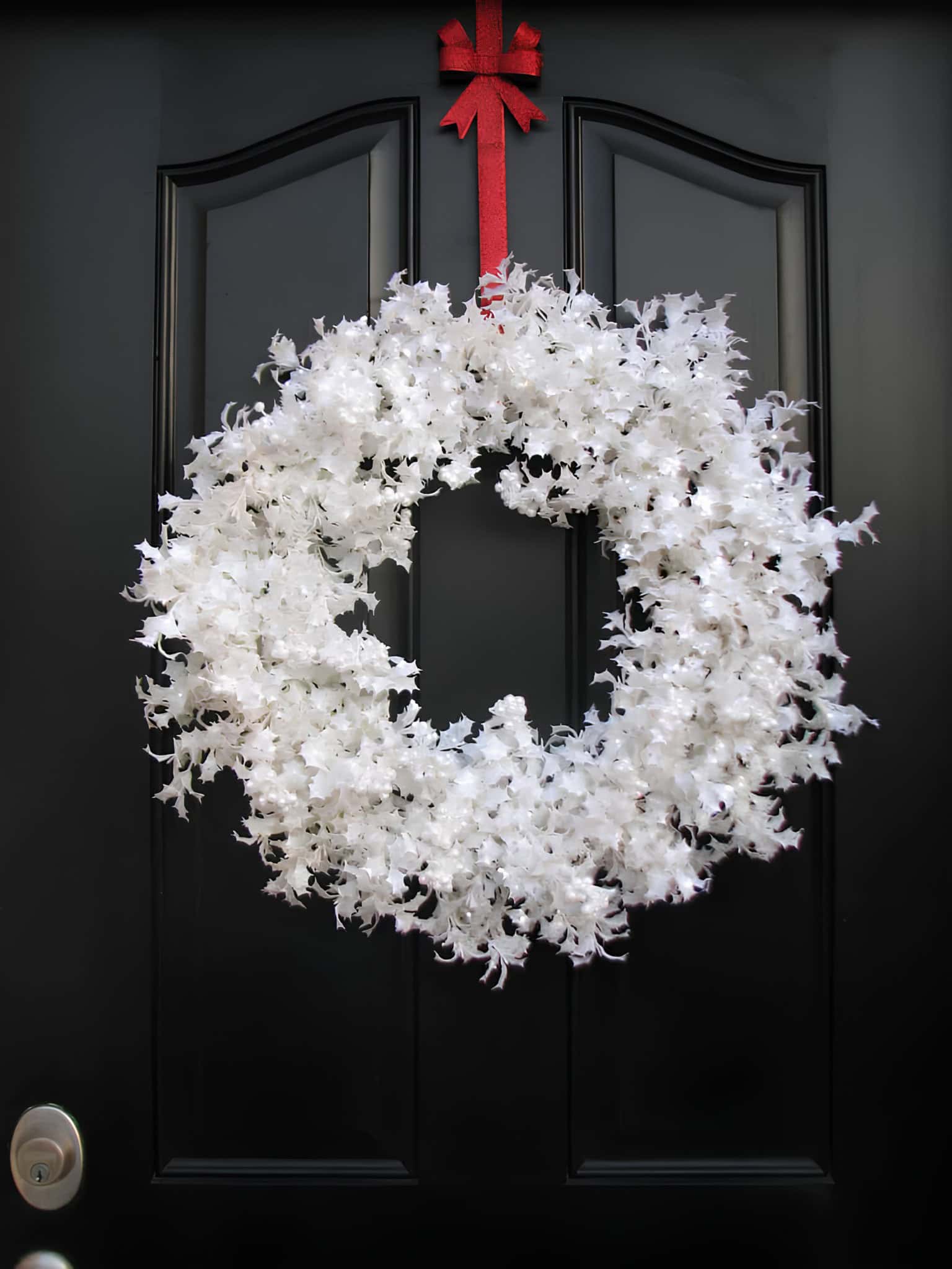 Classic white Christmas wreath with a bright red bow hanging on a dark door
