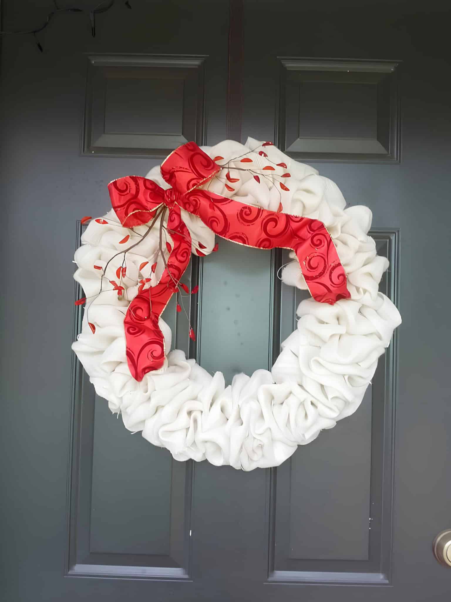 Elegant white Christmas wreath with a ruffled fabric texture and a bright red bow