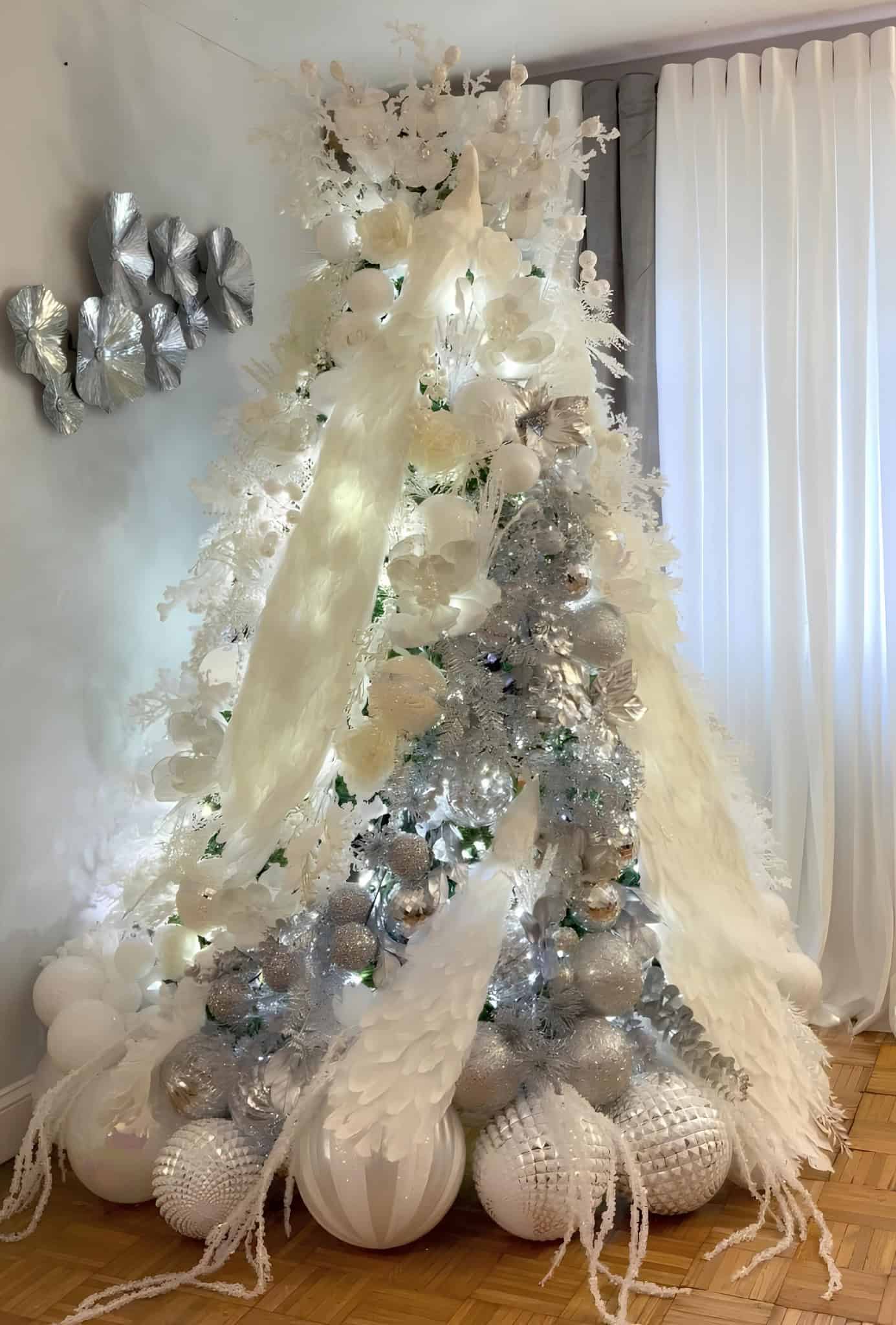 White and silver Christmas tree with angel wings, metallic ornaments, and glowing lights