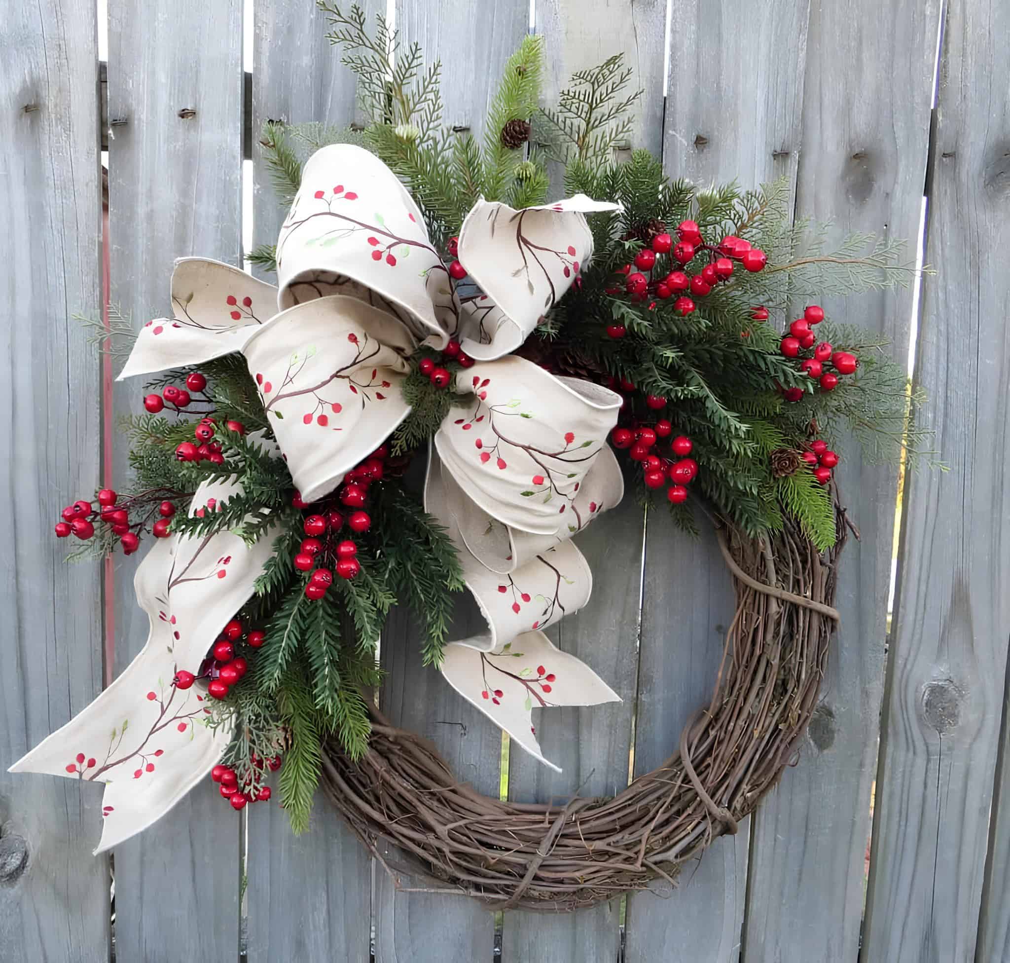 Wooden grapevine wreath with painted berry-branch ribbon, evergreens and red berries