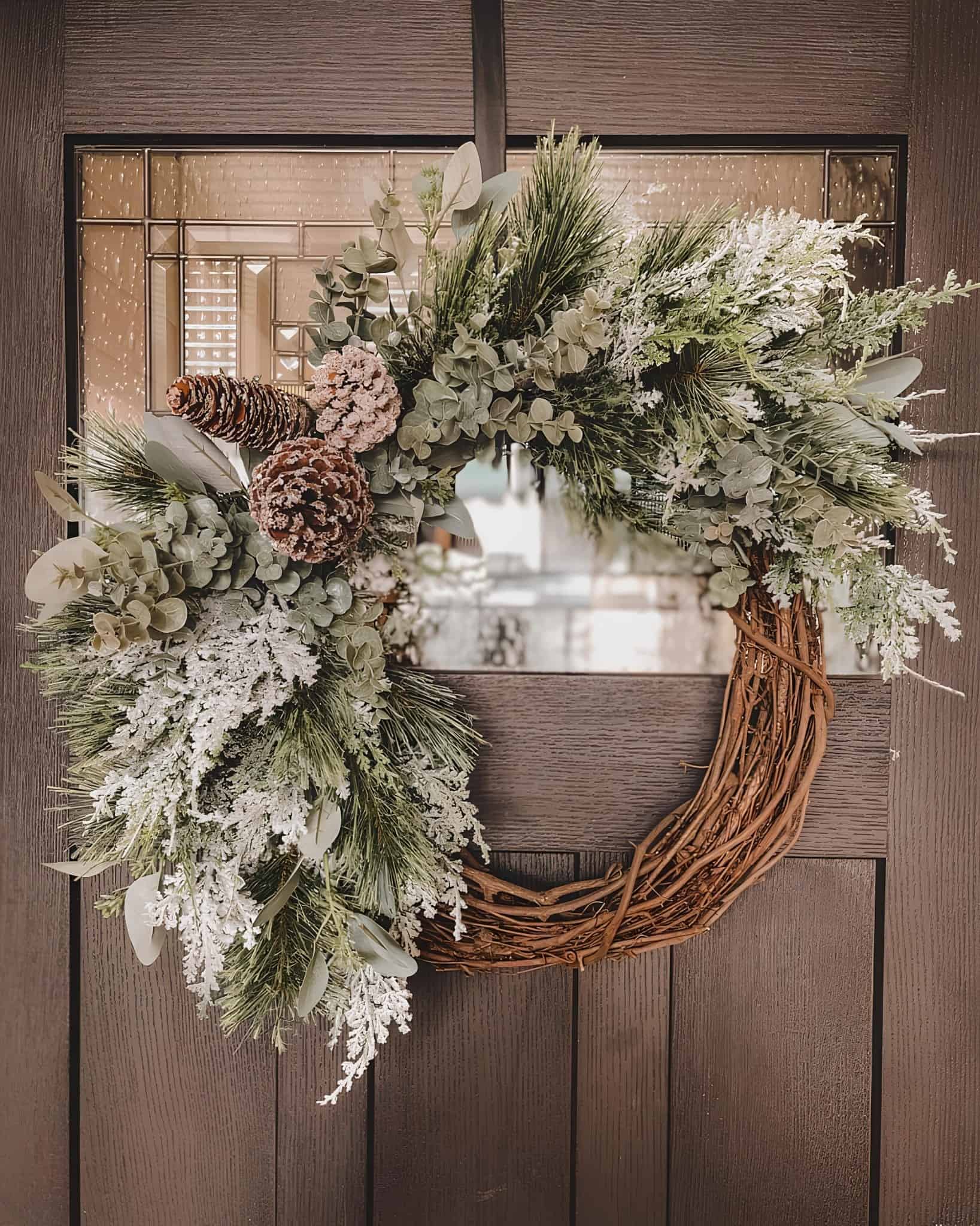 Half-covered wooden grapevine wreath with frosted eucalyptus, pine sprigs and snowy pinecones