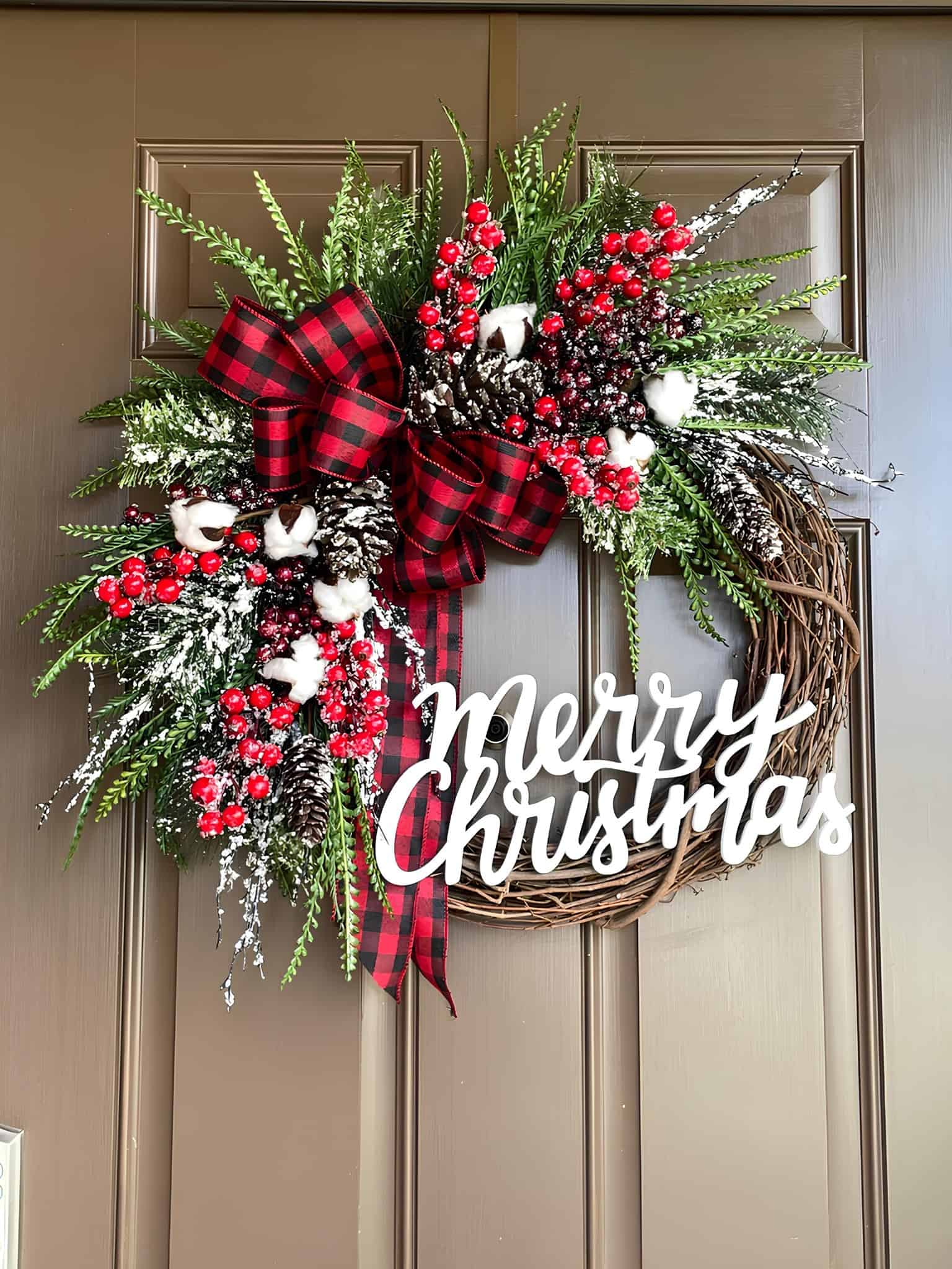 Wooden grapevine Christmas wreath with buffalo plaid bow, berries, snowy greens and a Merry Christmas sign
