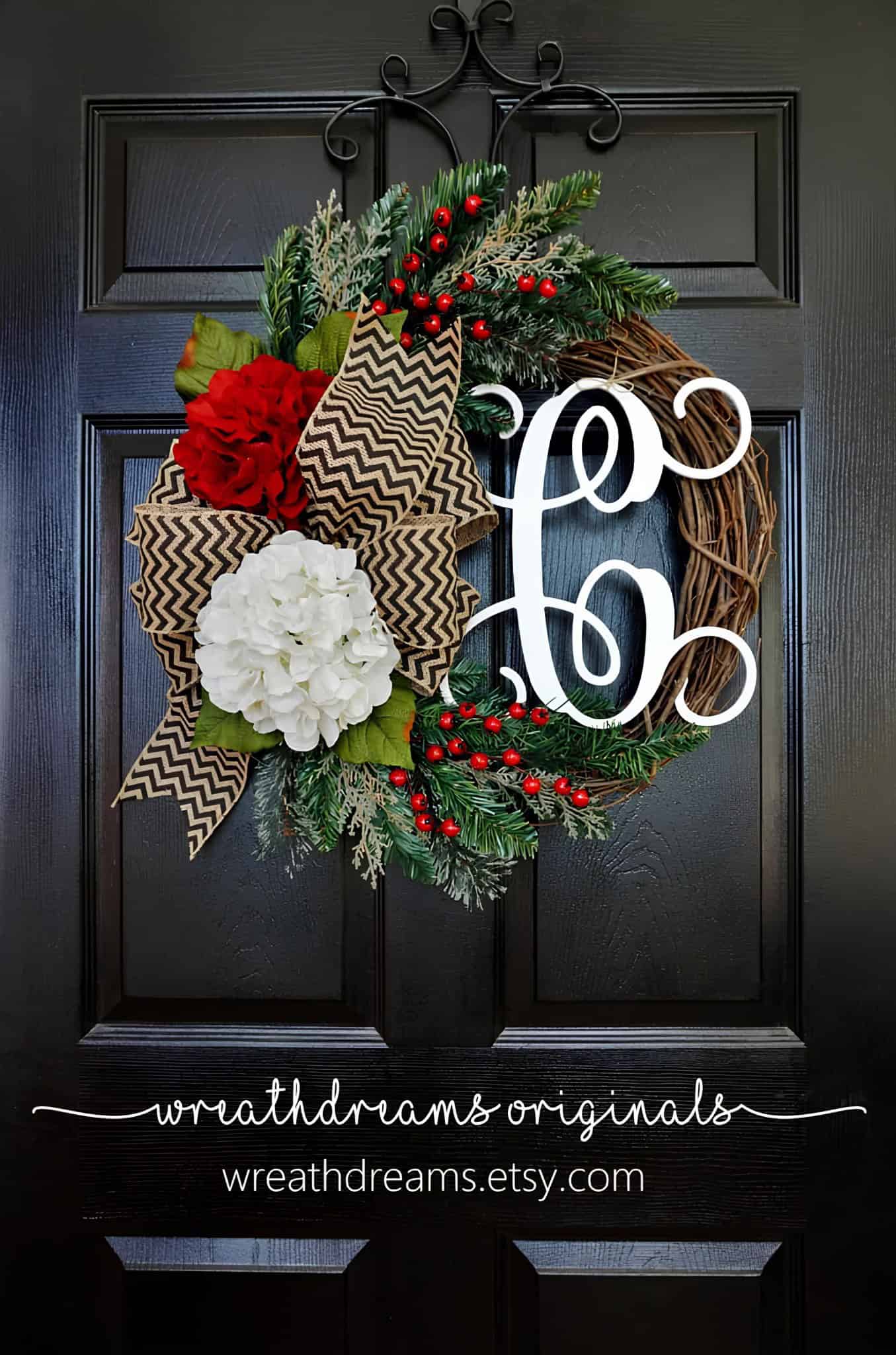 Vibrant holiday wreath with red and white flowers, greenery, and a modern "ho ho" sign, decorated with pinecones and berries, hanging on a black door for Christmas celebration.