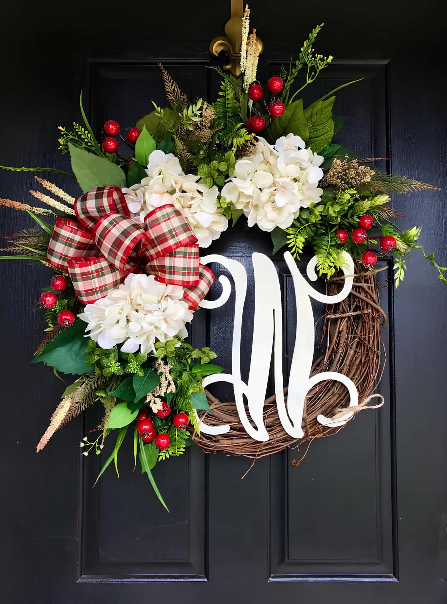Vibrant Christmas wreath with white hydrangeas, red berries, greenery, and a plaid bow hanging on a black door, decorated for the holiday season.