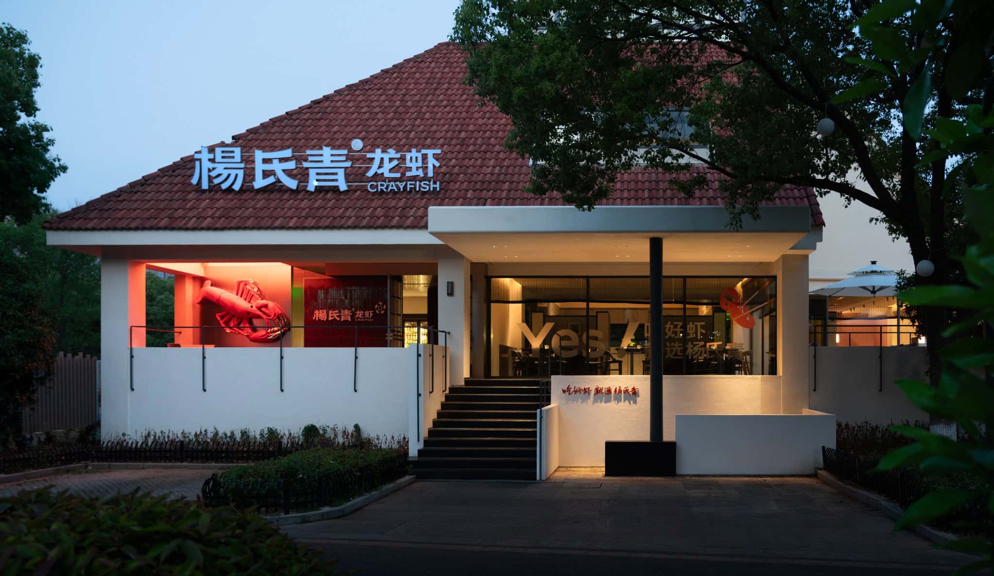 Crayfish restaurant exterior with modern architecture, illuminated signage, and outdoor seating area in the evening.