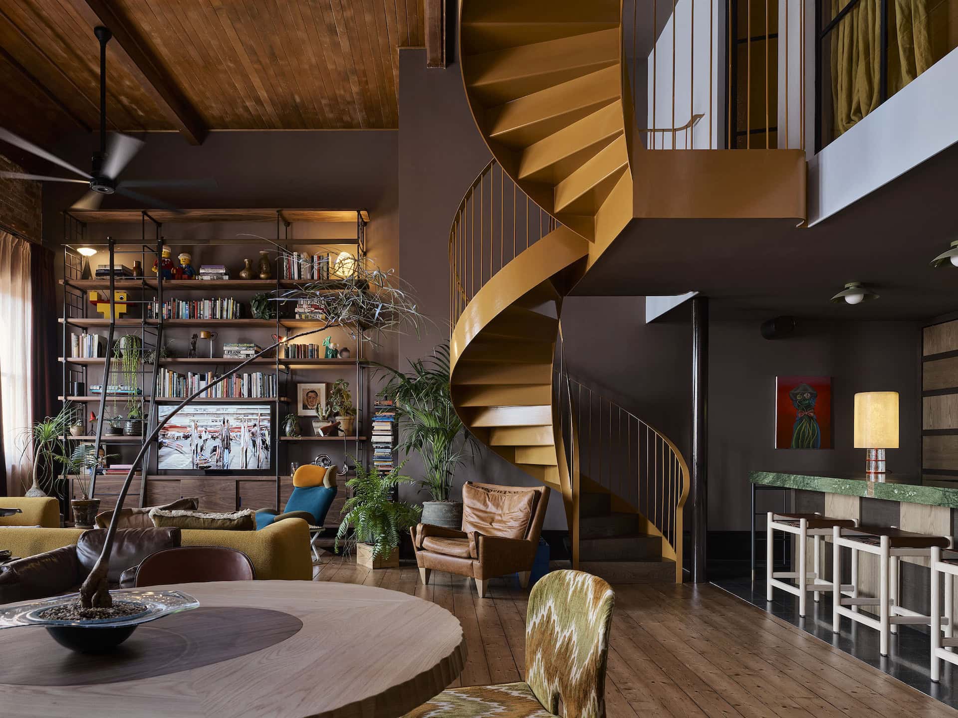Modern interior with a striking golden spiral staircase, eclectic furniture, and a cozy reading nook in a stylish living space showcasing contemporary architecture and interior design.