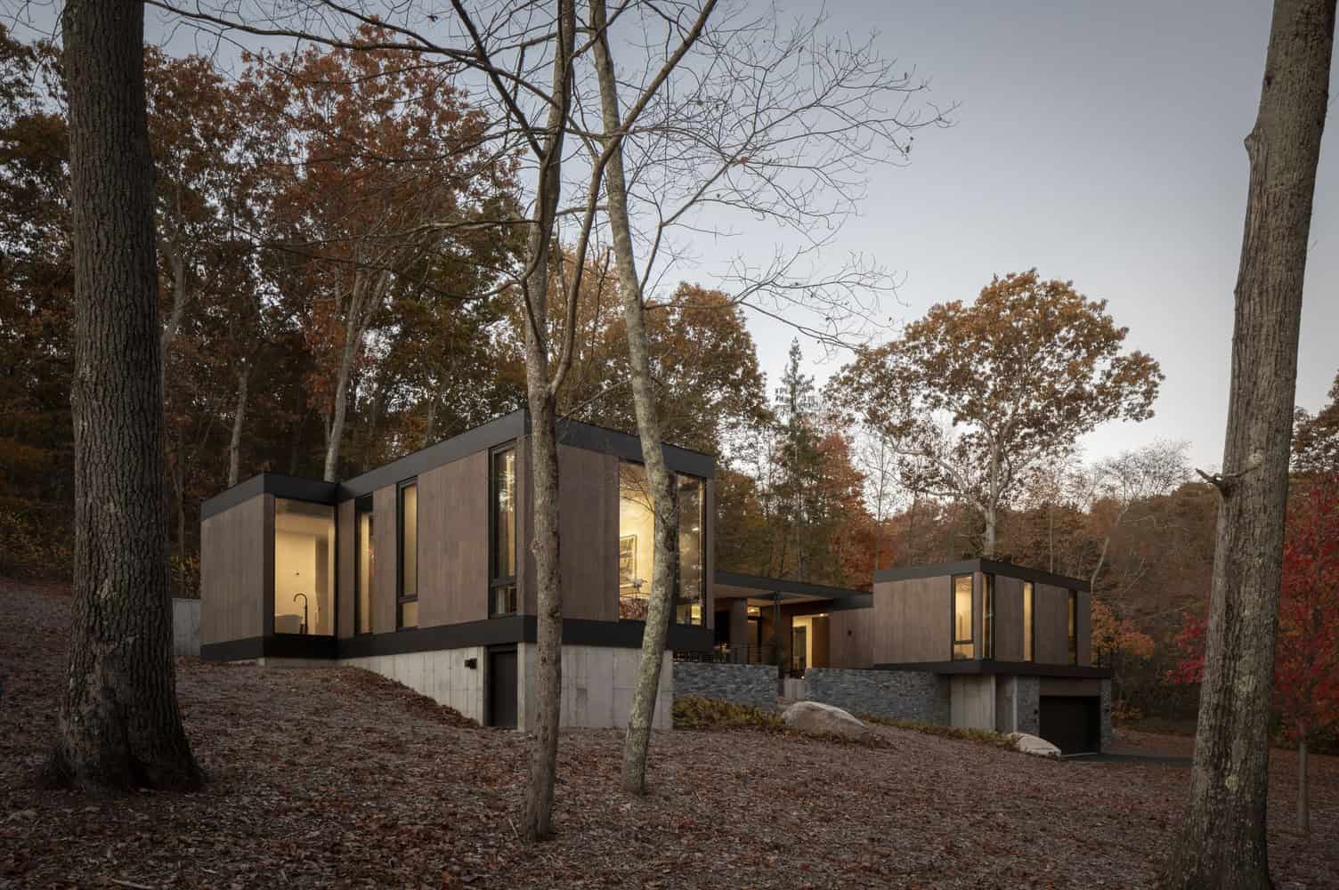 House in the Woods by Tom Lontine Architect, exterior at dusk stepping down woodland slope in Connecticut