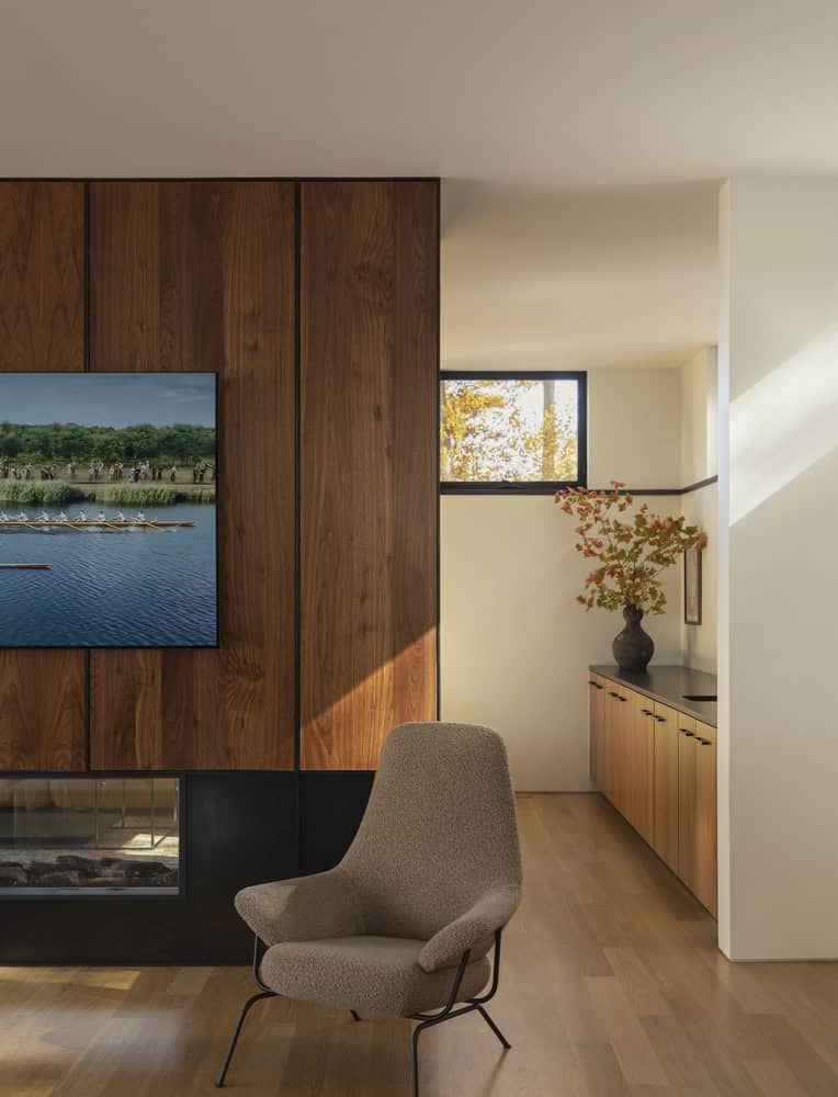 House in the Woods by Tom Lontine Architect, living room lounge chair by wood-paneled fireplace wall in Connecticut