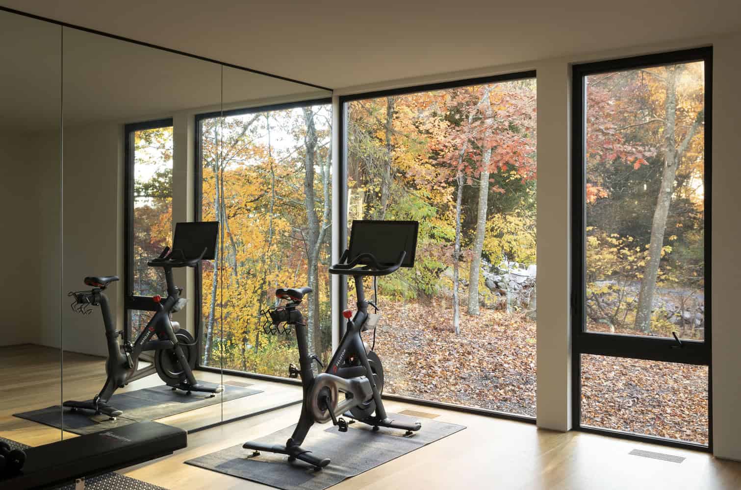 House in the Woods home gym with Peloton and full-height forest view windows in Connecticut by Tom Lontine Architect