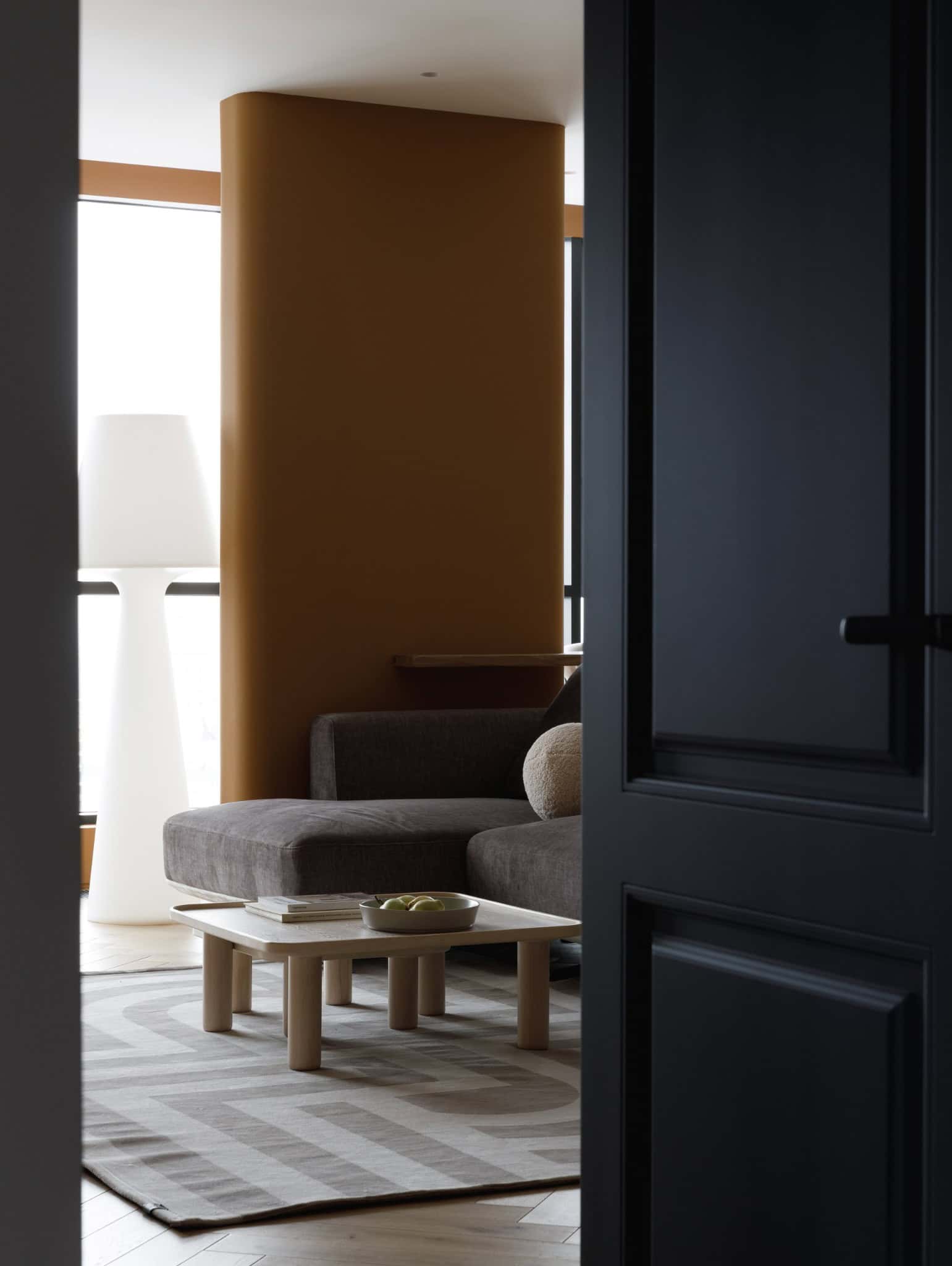 View into warm-toned living room with sofa and lamp in Lesoparkovy Apartment by STARIKOVA.ARCHITECTS