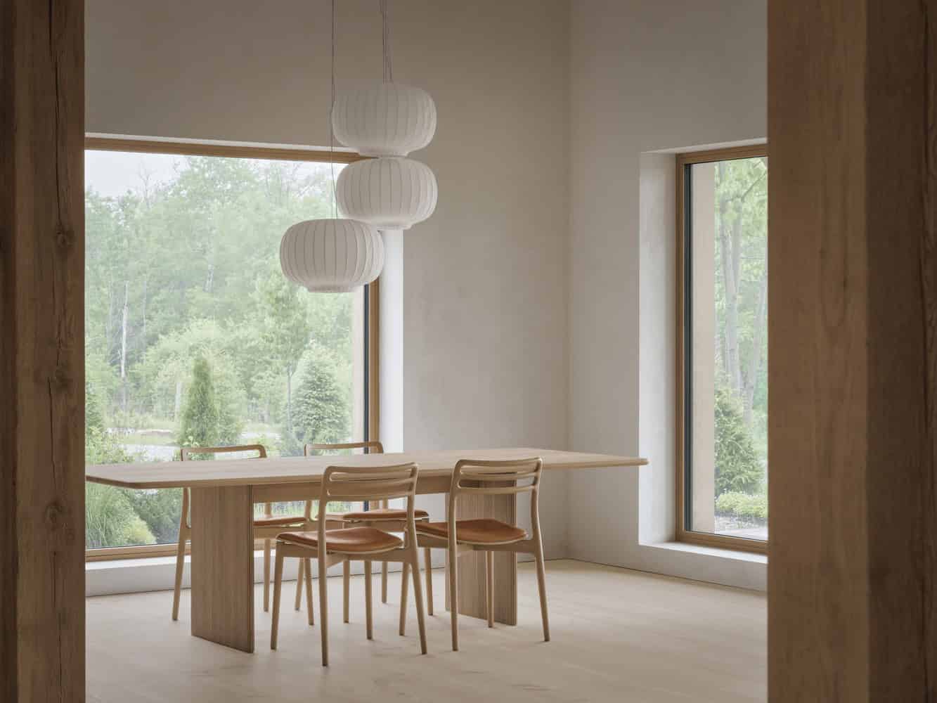 Maison Melba dining room by Atelier L’Abri with large landscape windows overlooking greenery in Frelighsburg, Quebec