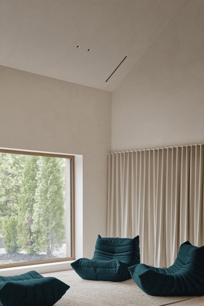 Maison Melba by Atelier L’Abri with green lounge chairs facing large picture window in Frelighsburg, Quebec